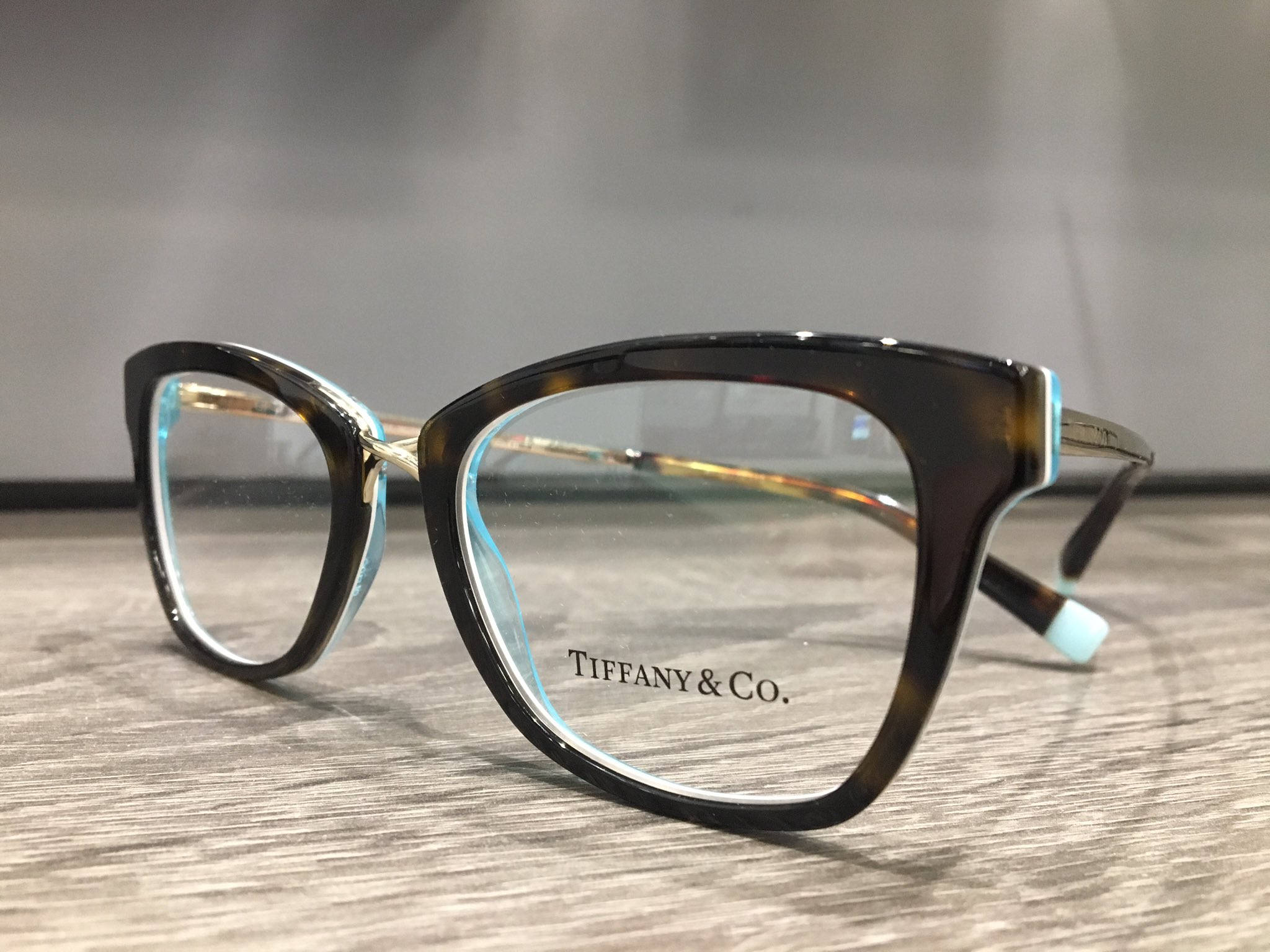 品牌 桌布 壁紙 — 優雅的玳瑁色Tiffany & Co.眼鏡，帶有淺藍色點綴，放置在木質表面上。