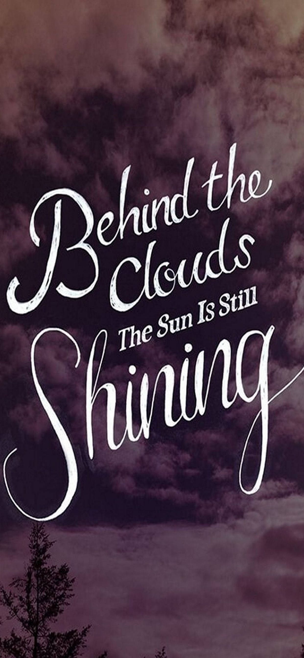 勵志 iPhone 桌布 壁紙 — 優雅的白色草書文字寫著「Behind the Clouds The Sun Is Still Shining」，背景是陰鬱的紫色多雲天空和孤獨的樹木剪影。