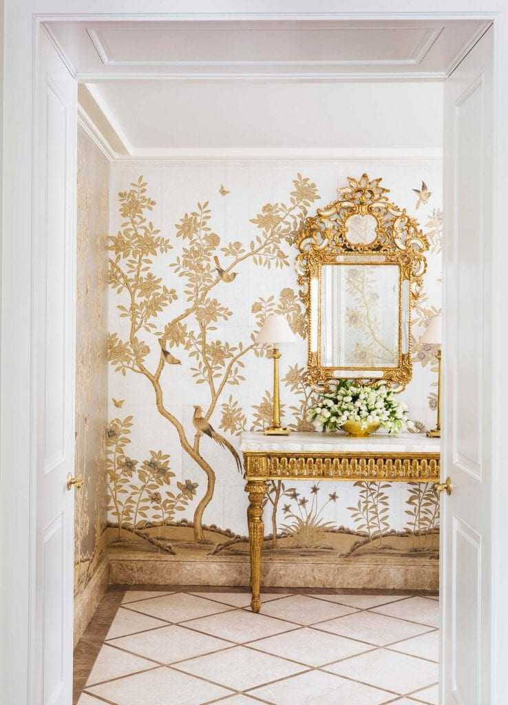 Chinoiserie 桌布 壁紙 — 優雅的走廊，飾有鳥和樹木的金箔壁紙、鍍金鏡子和大理石玄關桌，桌上擺放白色鮮花。