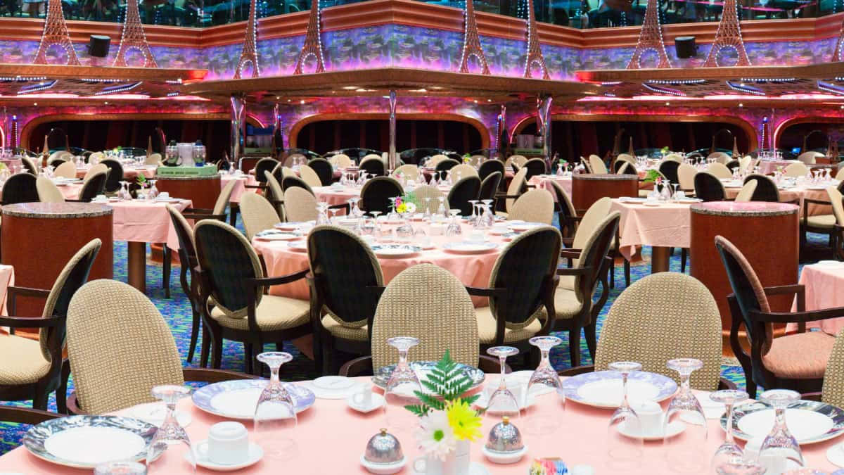 Carnival Conquest 桌布 壁紙 — 優雅的郵輪餐廳，圓桌在閃爍的水晶燈和鮮豔的粉紅色桌布下為精緻晚餐準備就緒。