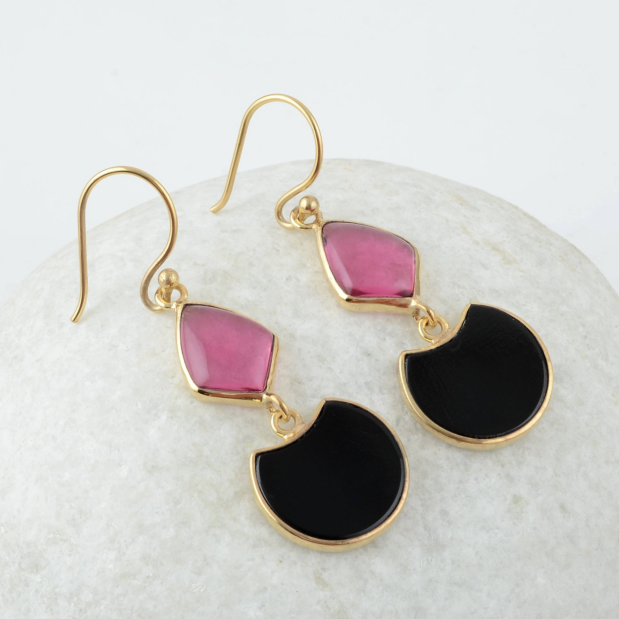 Gold Jewellery 桌布 壁紙 — 優雅的金色耳環，帶有粉紅色和黑色石頭水滴，放置在光滑的白色大理石表面上。