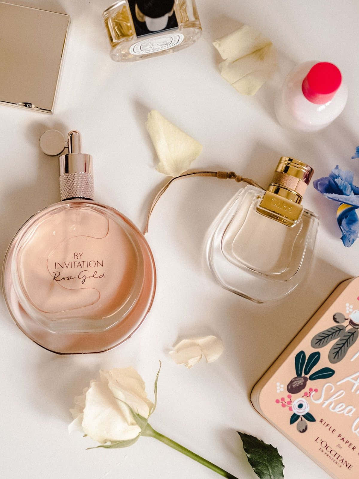 Spring Perfume 桌布 壁紙 — 優雅的香水瓶和玫瑰花瓣整齊地擺放在潔白的表面上，柔和自然光線照射。