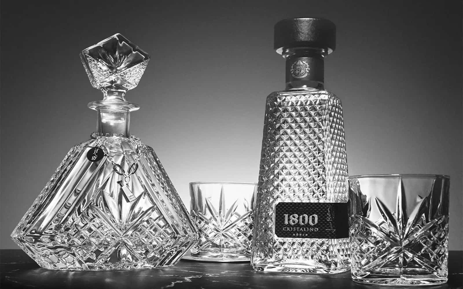 alcohol 桌布 壁紙 — 優雅的黑白靜物，展示標有1800 Cristalino的水晶醒酒瓶及配套酒杯，置於深色大理石檯面上。