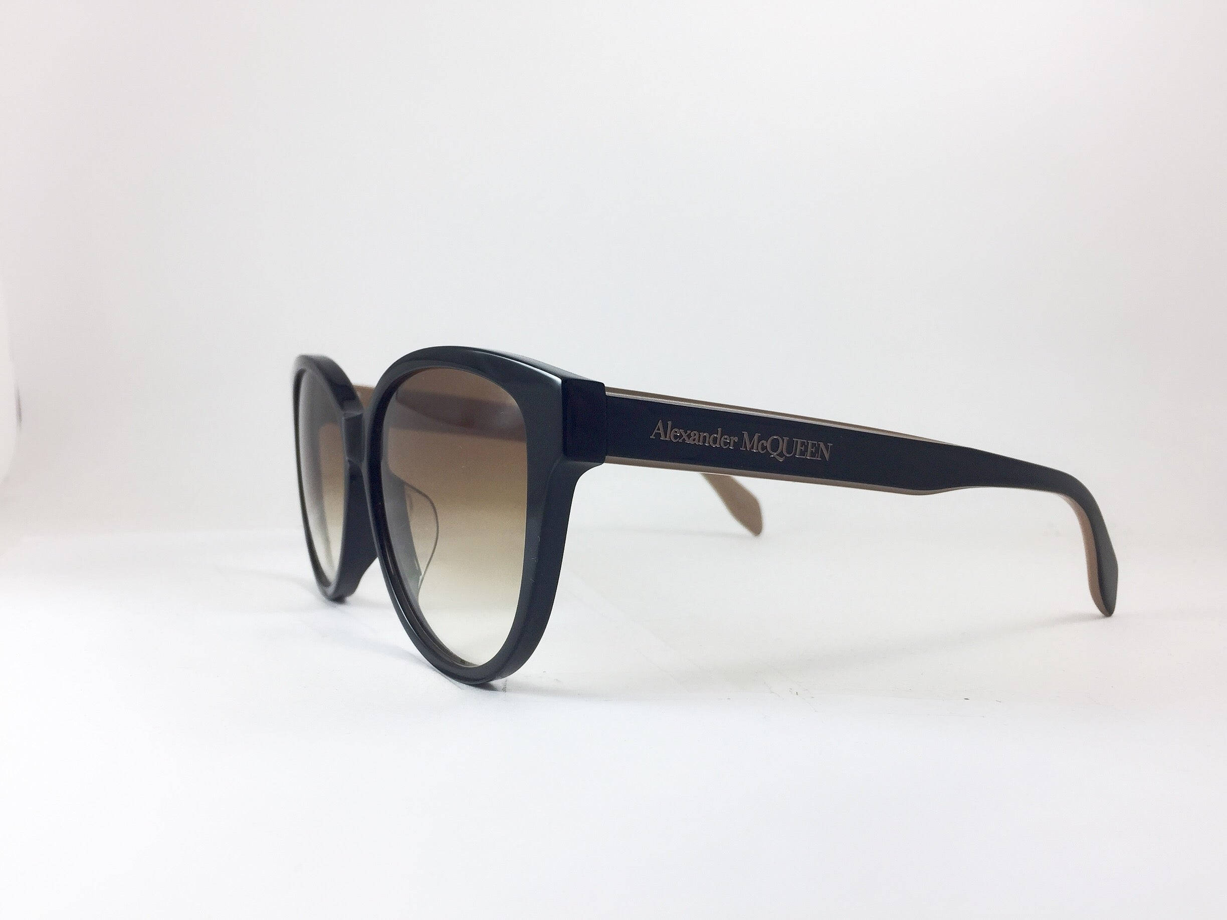 Sunglasses 桌布 壁紙 — 優雅的黑色Alexander McQueen太陽眼鏡，配備棕色漸變鏡片，放置在純白表面上。