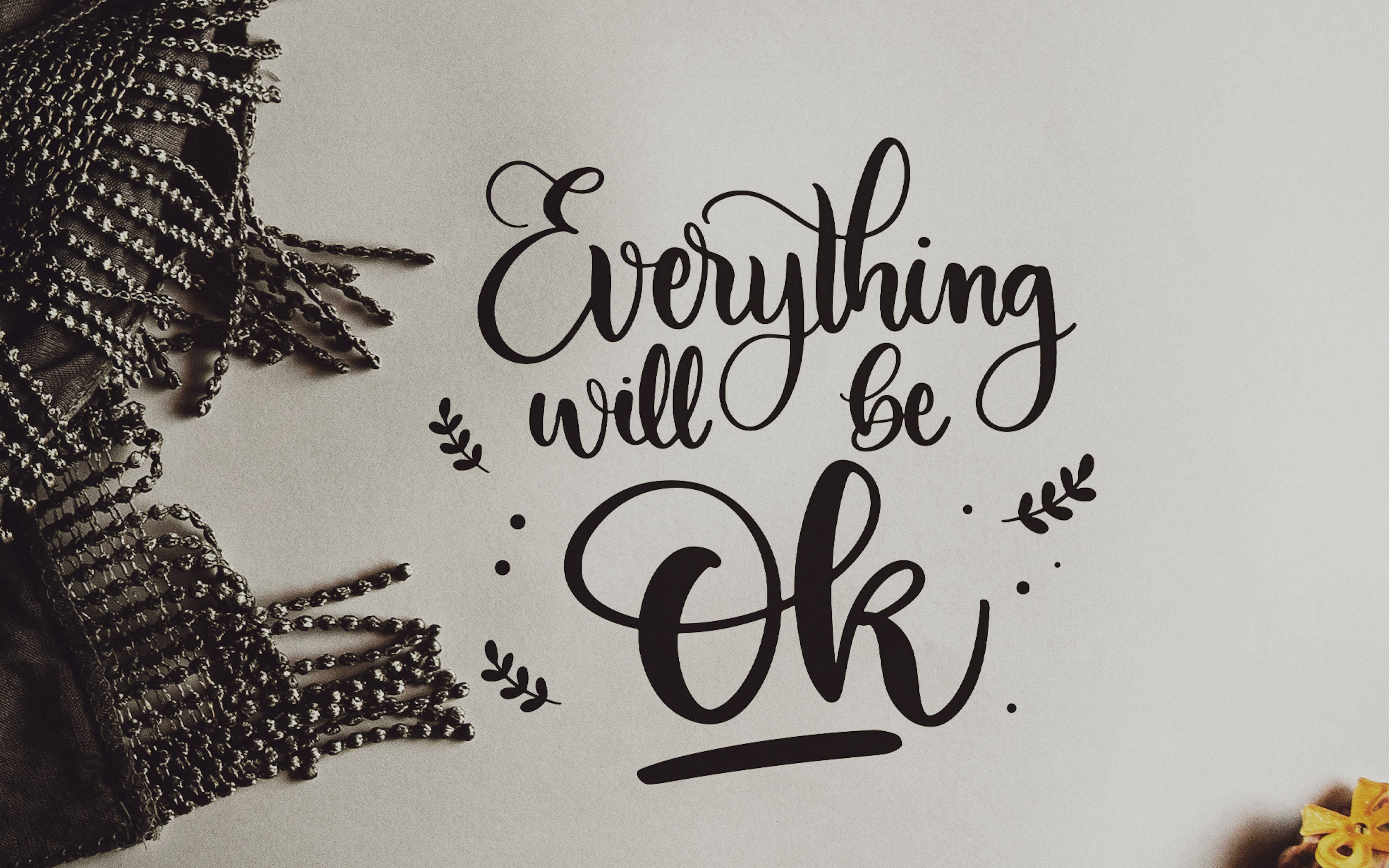桌布 壁紙 — 優雅的黑色書法在柔軟的灰色表面上寫著「Everything will be Ok」，旁邊有一條珠飾黑色圍巾和一朵黃花。