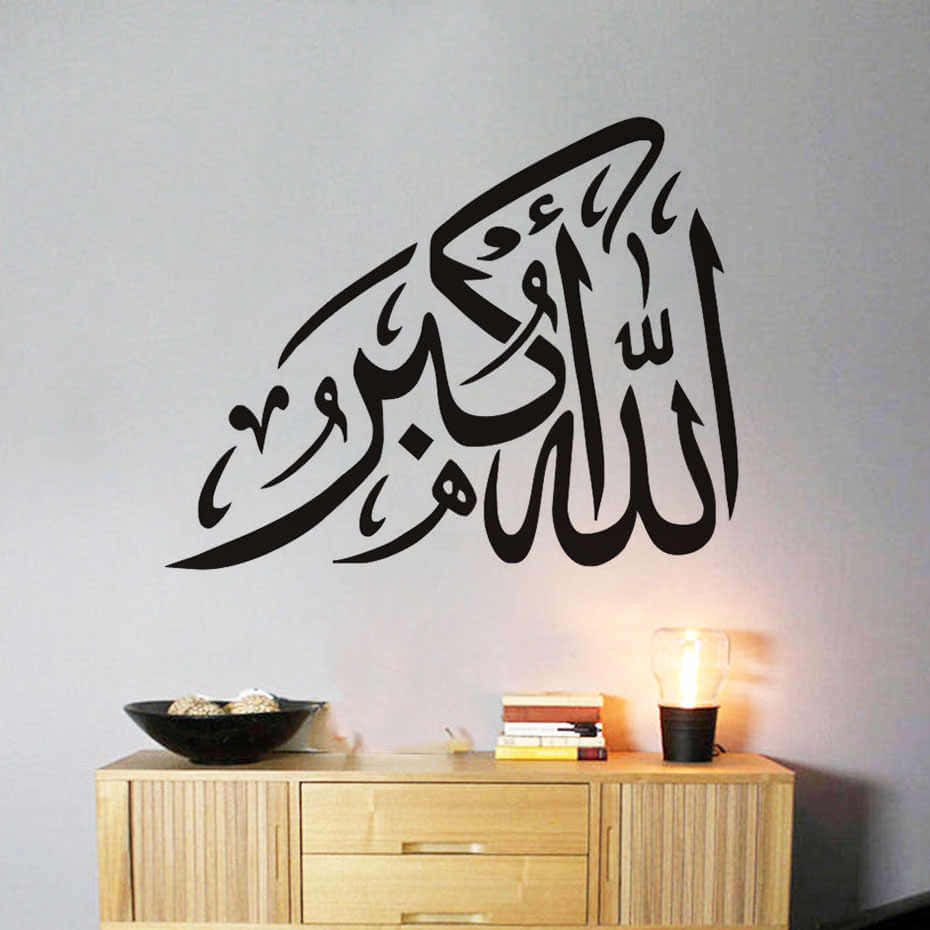 arabic 桌布 壁紙 — 優雅的黑色阿拉伯書法牆貼，位於木櫃上方，配有一盞發光的燈和堆疊的書籍。