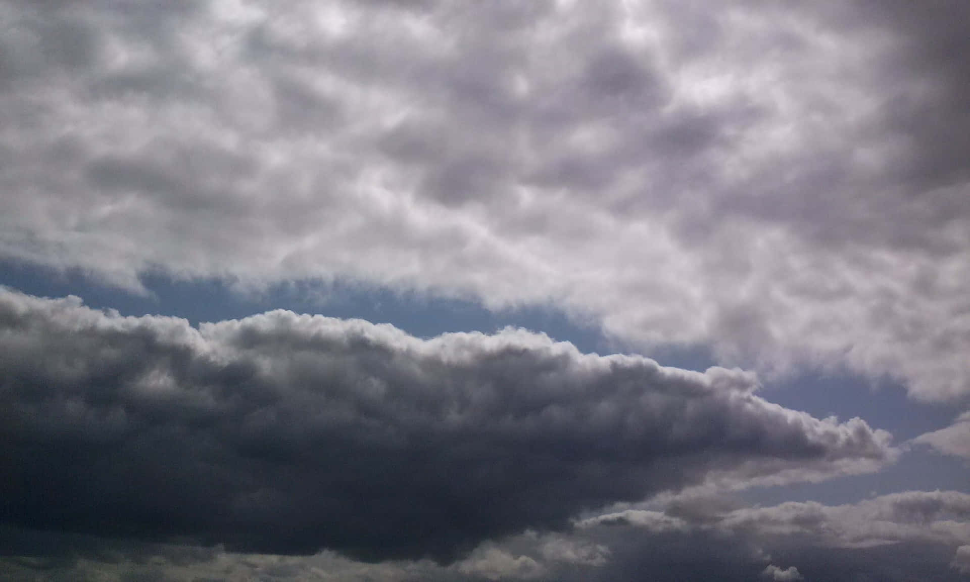 STORM-1 壁紙 — 充滿層次感的戲劇性天空，雲層從柔和的灰色到深炭灰色，並有藍色隱約透出。