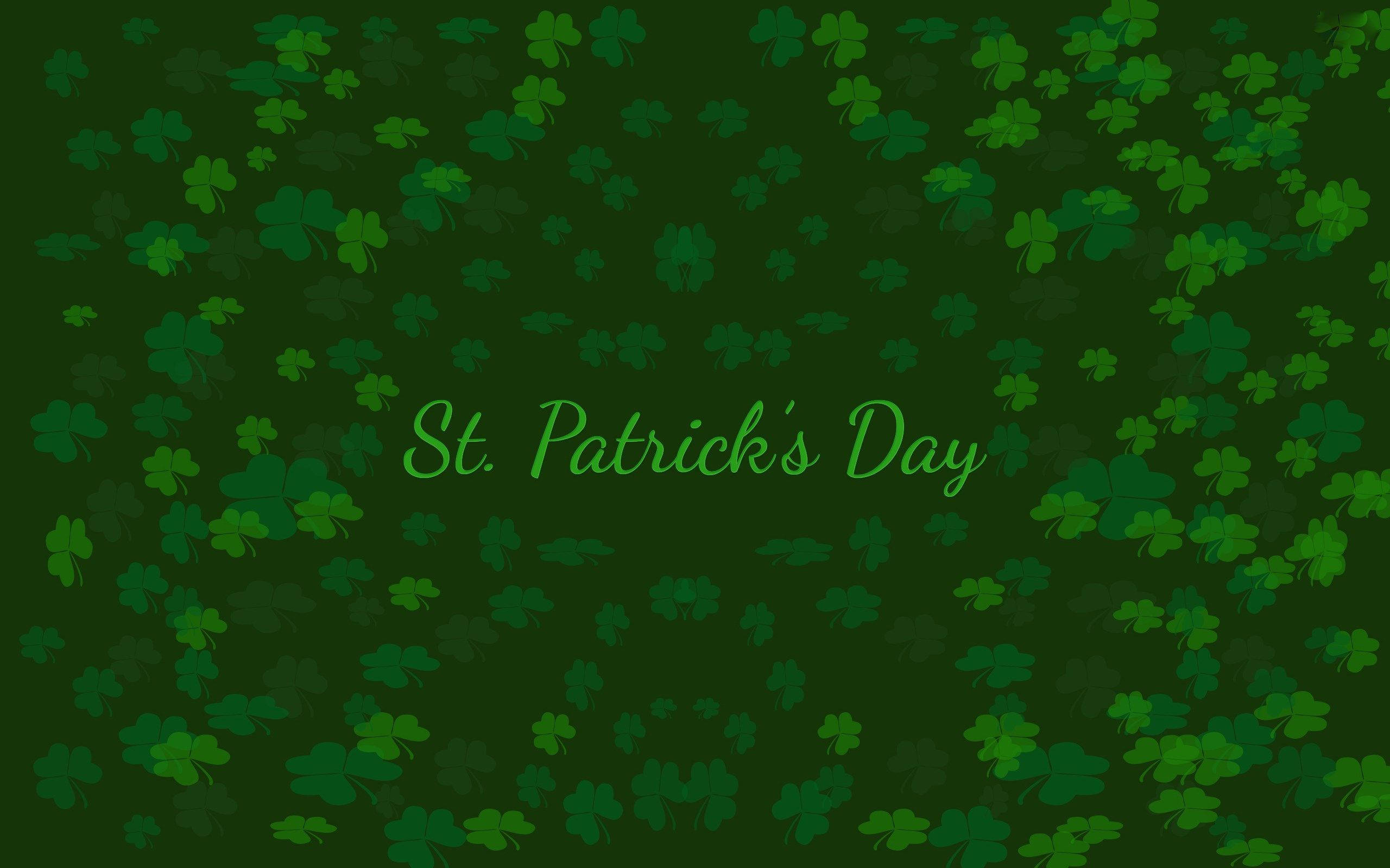 St Patrick's Day 桌布 壁紙 — 充滿散落三葉草和草書聖派翠克節文字的節日綠色背景。