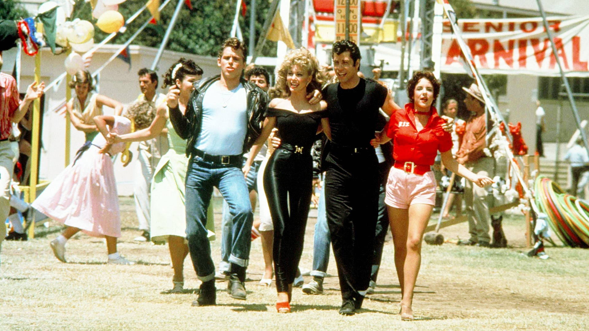 Grease 桌布 壁紙 — 充滿活力的1950年代高中舞會場景，青少年在明亮的嘉年華燈光下跳舞和擺姿勢。