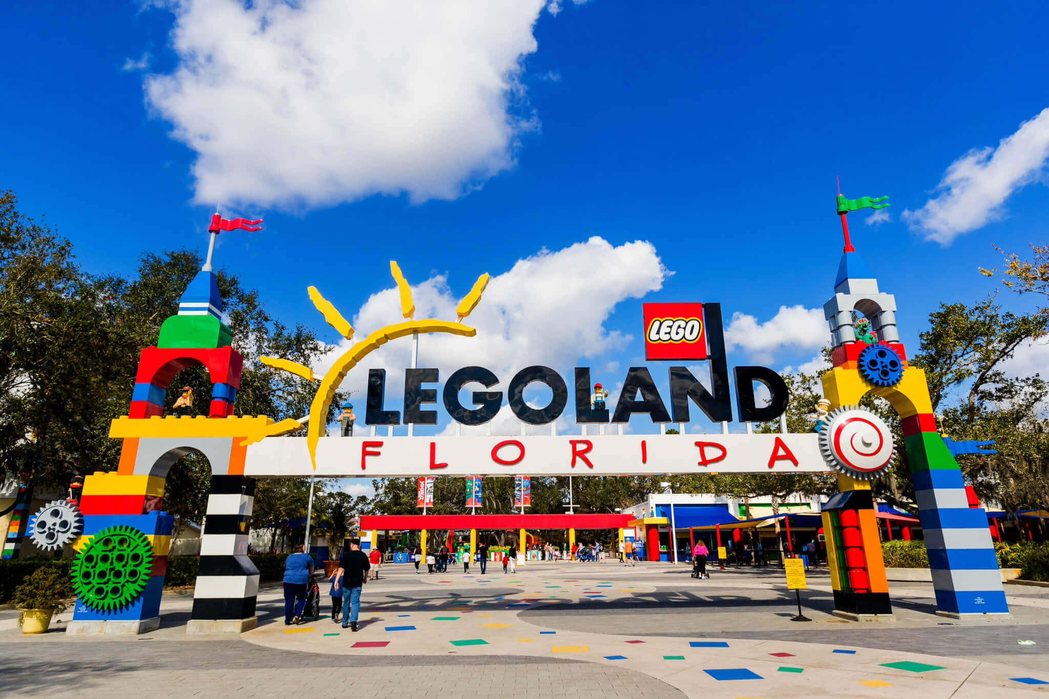 Legoland 桌布 壁紙 — 充滿活力的LEGO主題入口拱門，色彩繽紛的積木塔和微笑的太陽在明亮的藍天下。