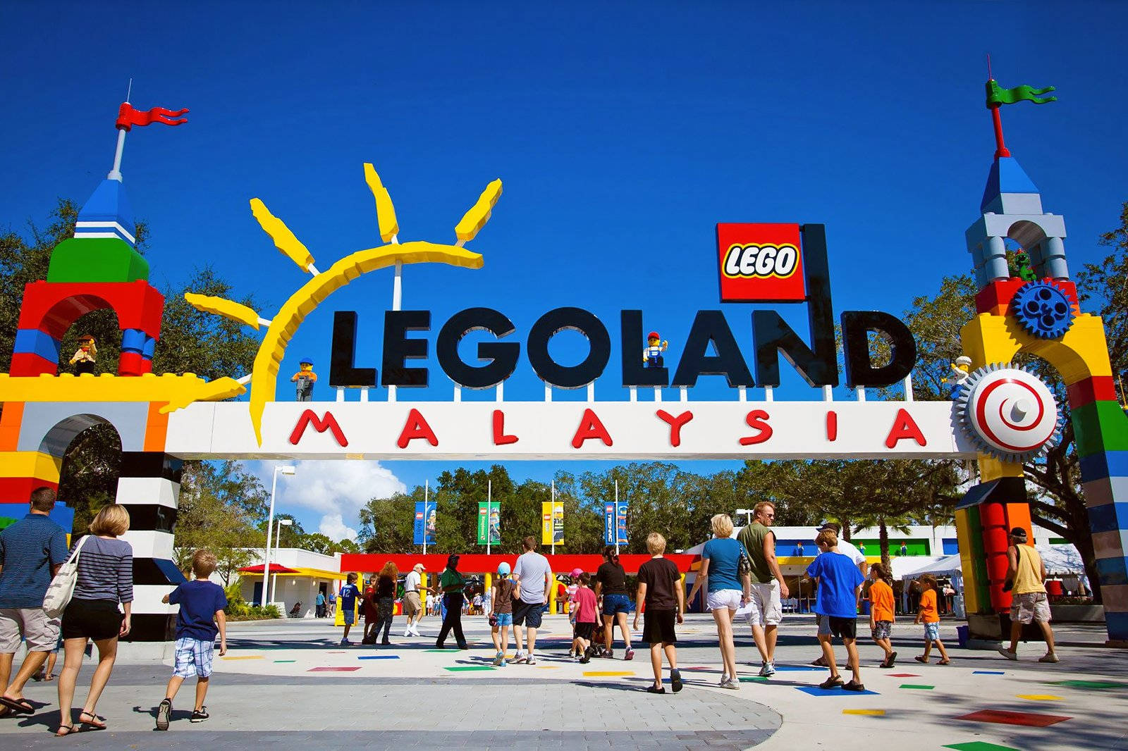 小孩動圖 桌布 壁紙 — 充滿活力的LEGO主題入口拱門，色彩繽紛的積木塔和微笑的遊客在晴朗的藍天下。