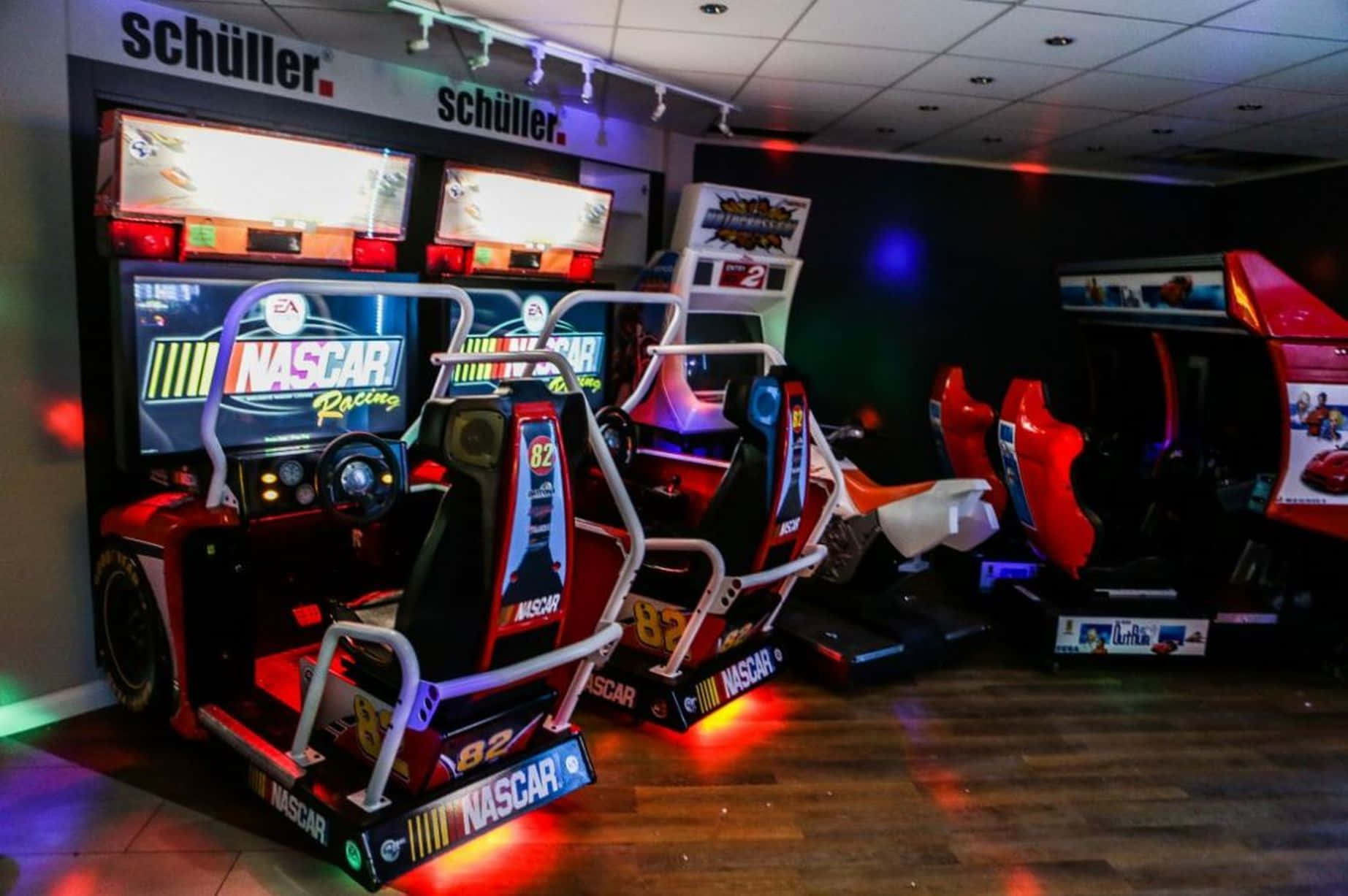 Arcade Games 桌布 壁紙 — 充滿活力的NASCAR賽車街機在昏暗的遊戲室中，在色彩繽紛的霓虹燈下閃耀。