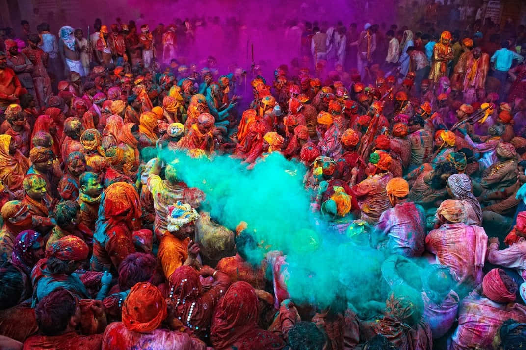 Holi 桌布 壁紙 — 充滿活力的人群沉浸在五彩斑斕的粉末中，慶祝侯麗節，旋轉的藍綠色塵埃佔據中心位置。