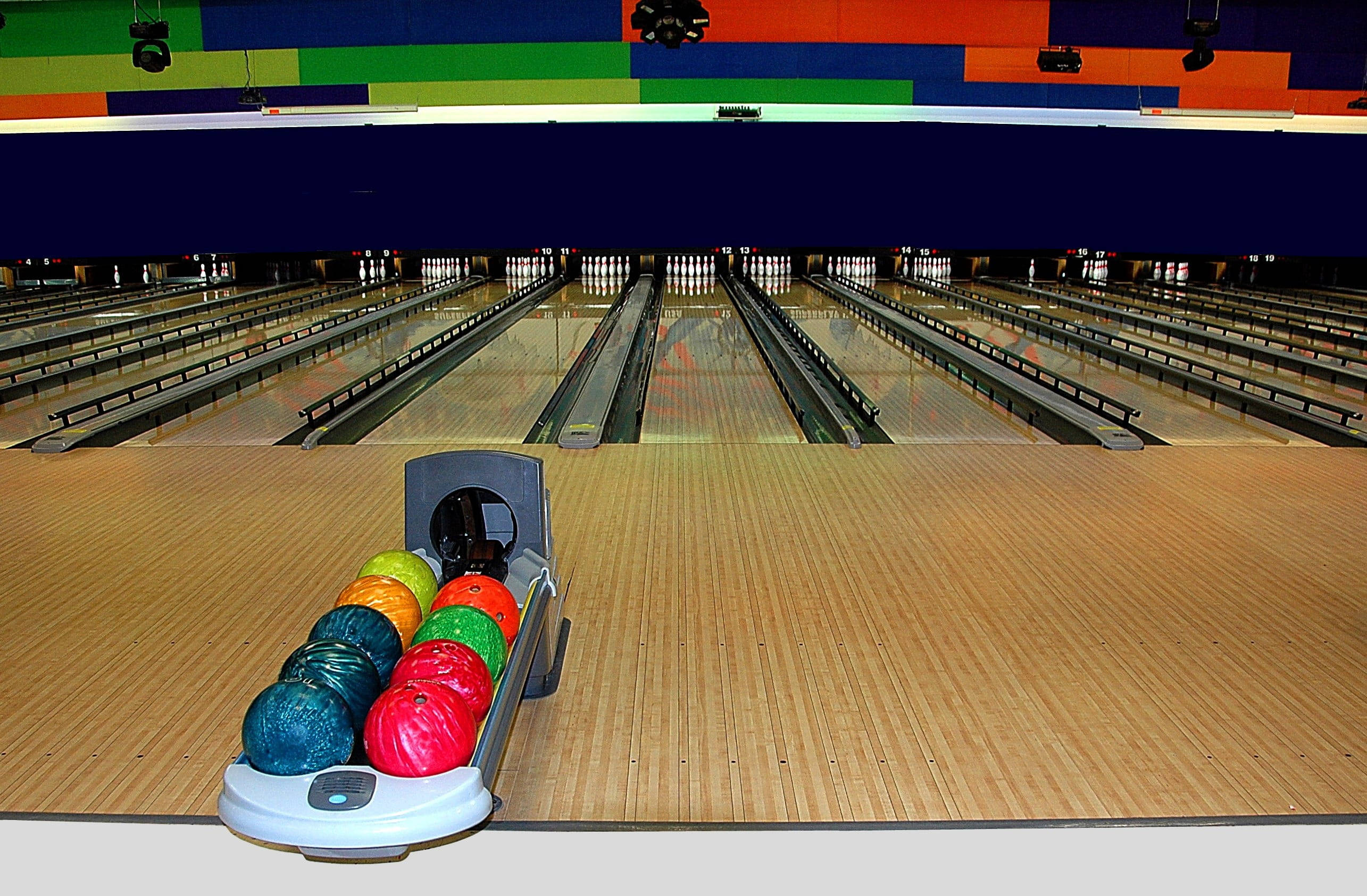 Bowling 桌布 壁紙 — 充滿活力的保齡球道，彩色保齡球在多彩牆壁下的回球架上排列整齊。
