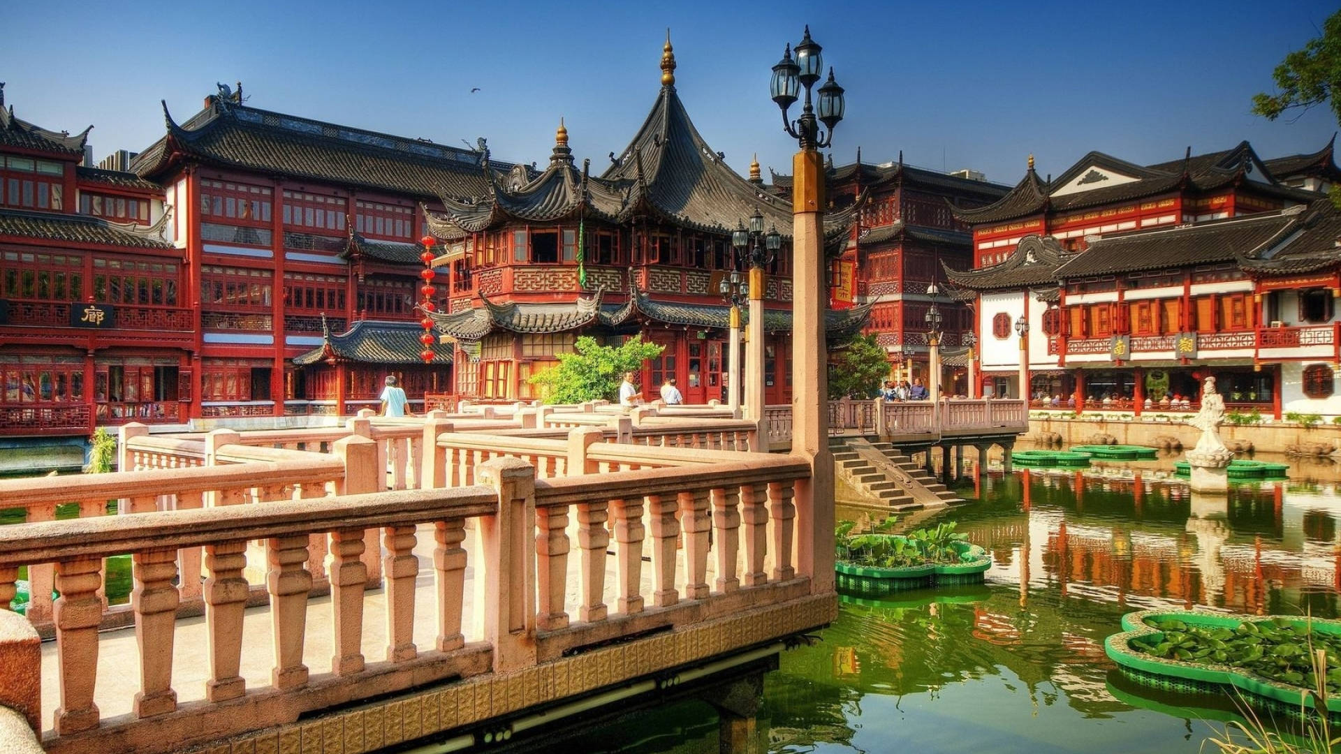 Shanghai 桌布 壁紙 — 充滿活力的傳統中式庭院，紅色建築、黑色屋頂、綠色池塘上的石橋，在清澈的藍天下。
