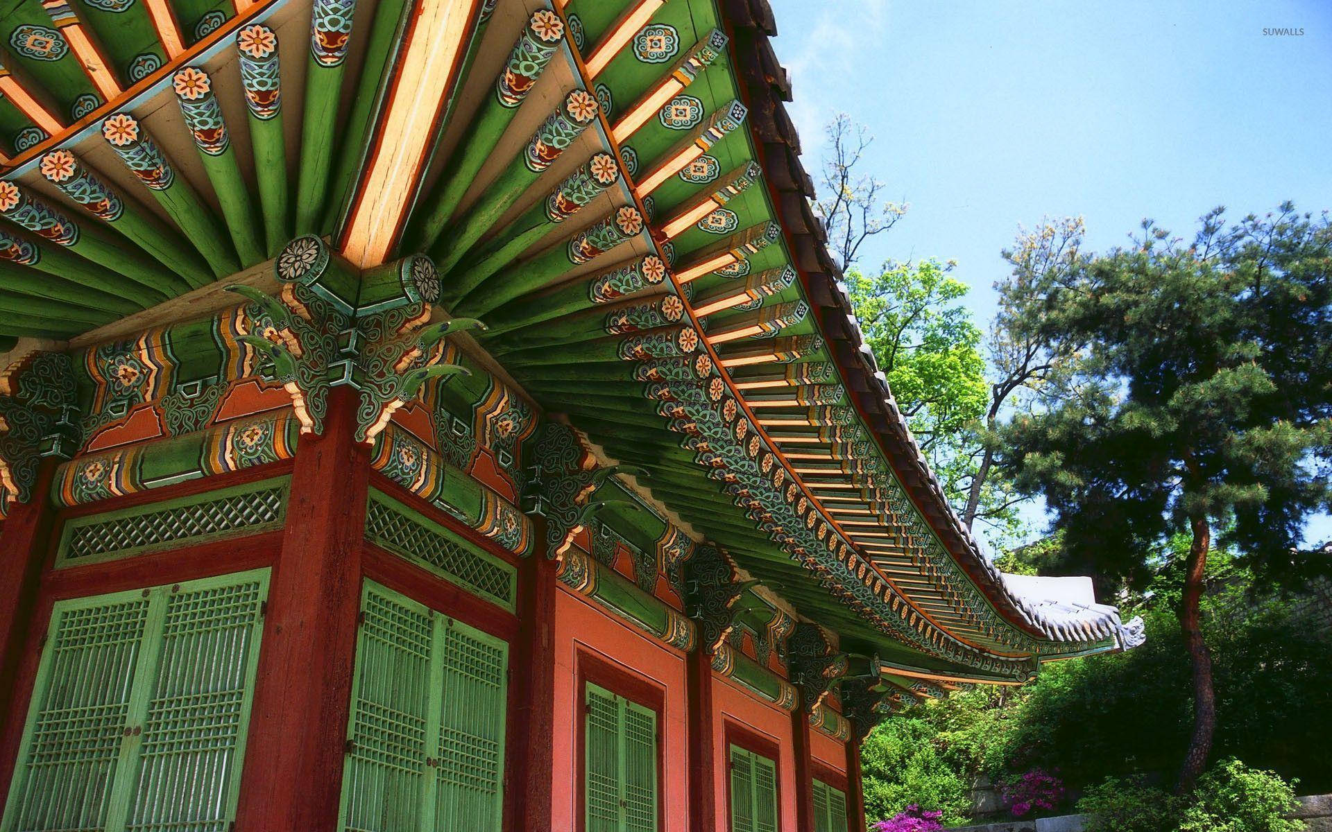 南韓 桌布 壁紙 — 充滿活力的傳統韓國寺廟屋頂，帶有複雜的綠色、橙色和紅色圖案，映襯著清澈的藍天和茂密的綠樹。