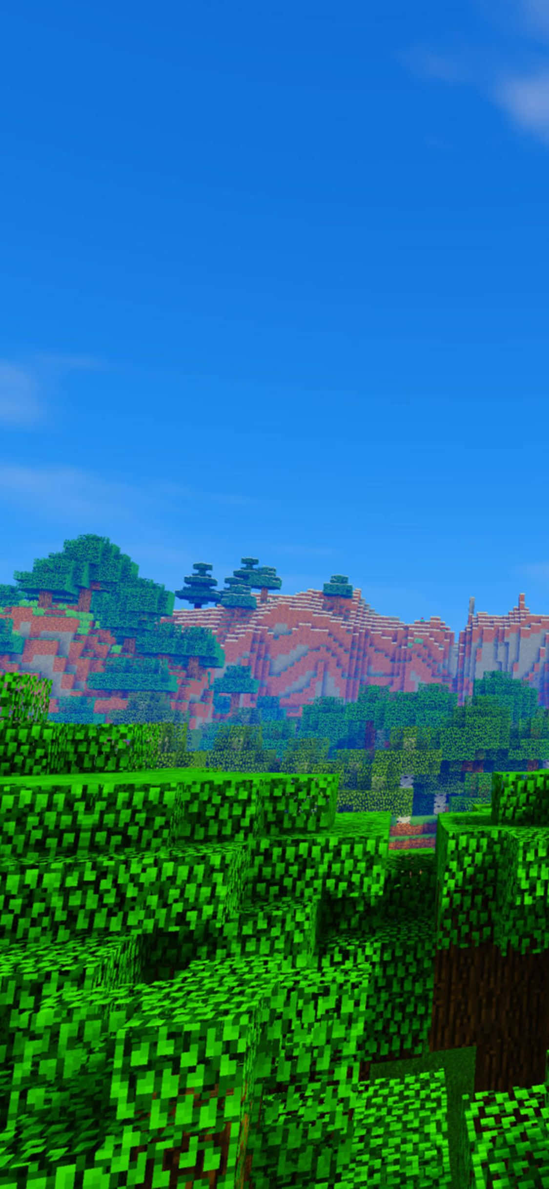 iPhone Xs Minecraft 桌布 壁紙 — 充滿活力的像素化Minecraft景觀，茂密的綠色樹木和紅色條紋山脈，在清澈的藍天下。