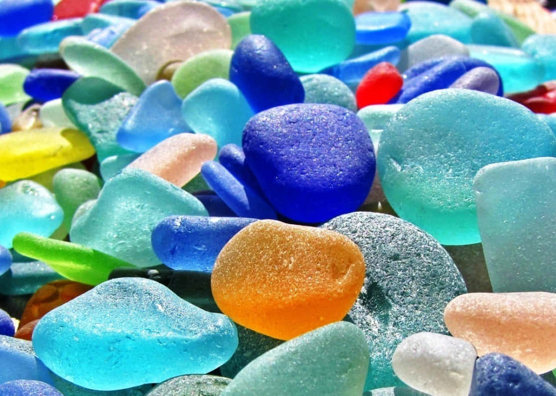 Sea Glass 桌布 壁紙 — 充滿活力的光滑海玻璃卵石，呈現藍色、綠色、黃色和橙色，在明亮的陽光下閃閃發光。