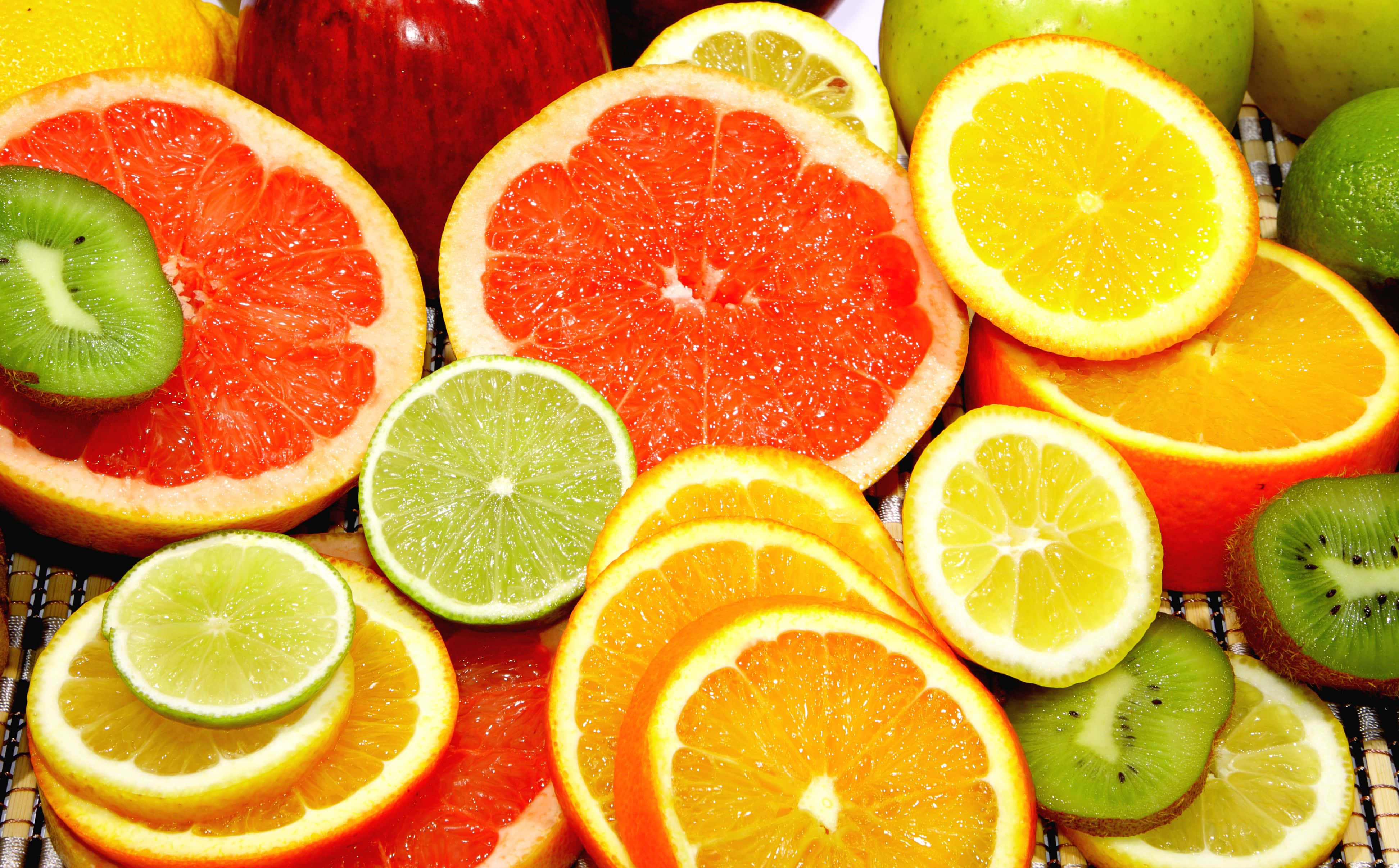 Fruit 桌布 壁紙 — 充滿活力的切片柑橘類水果和完整水果，如西柚、奇異果和柳橙，排列在編織墊上。