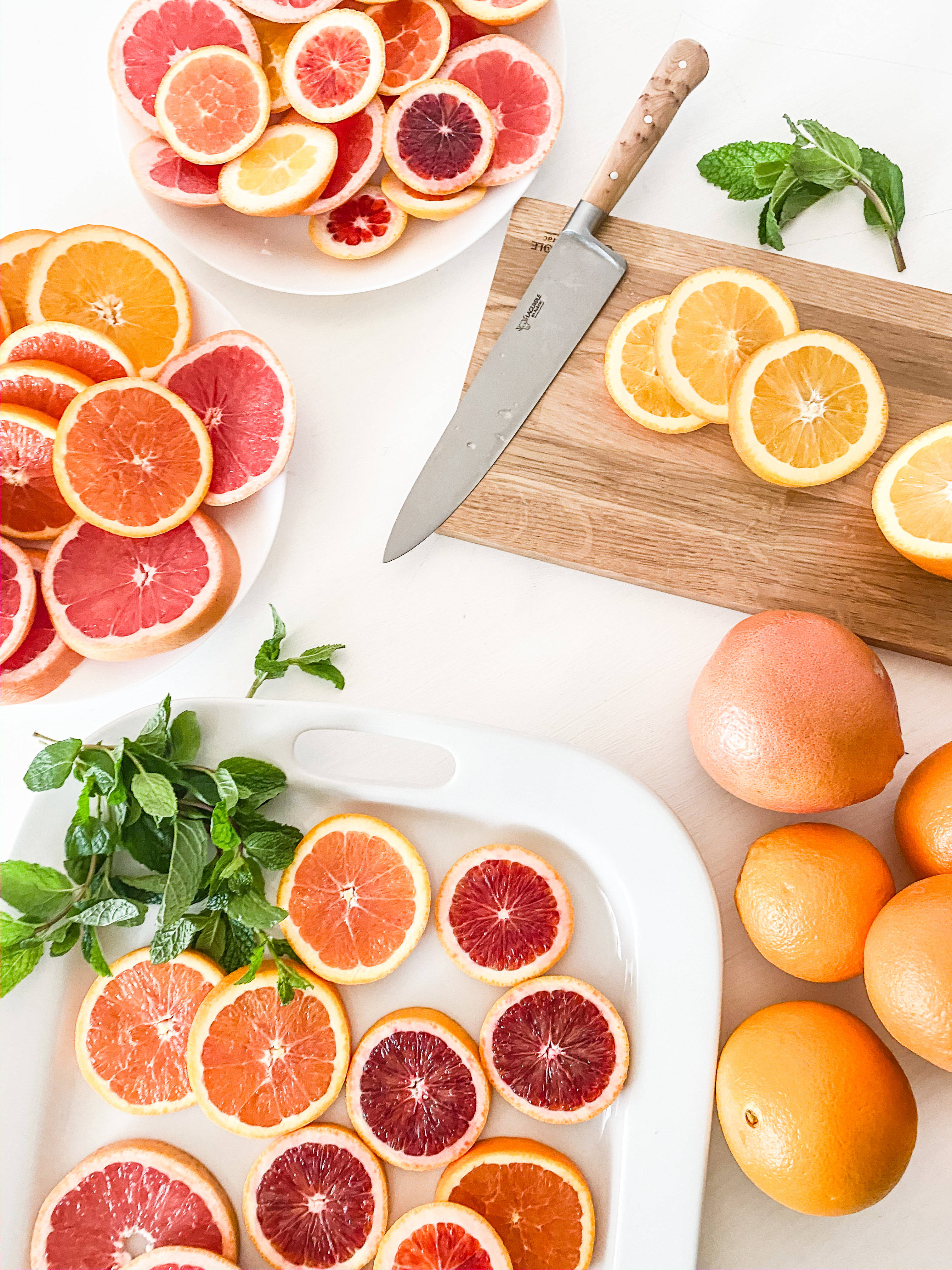 Fruit 桌布 壁紙 — 充滿活力的切片葡萄柚和柳橙排列在白盤和木砧板上，配以新鮮薄荷和一把刀。
