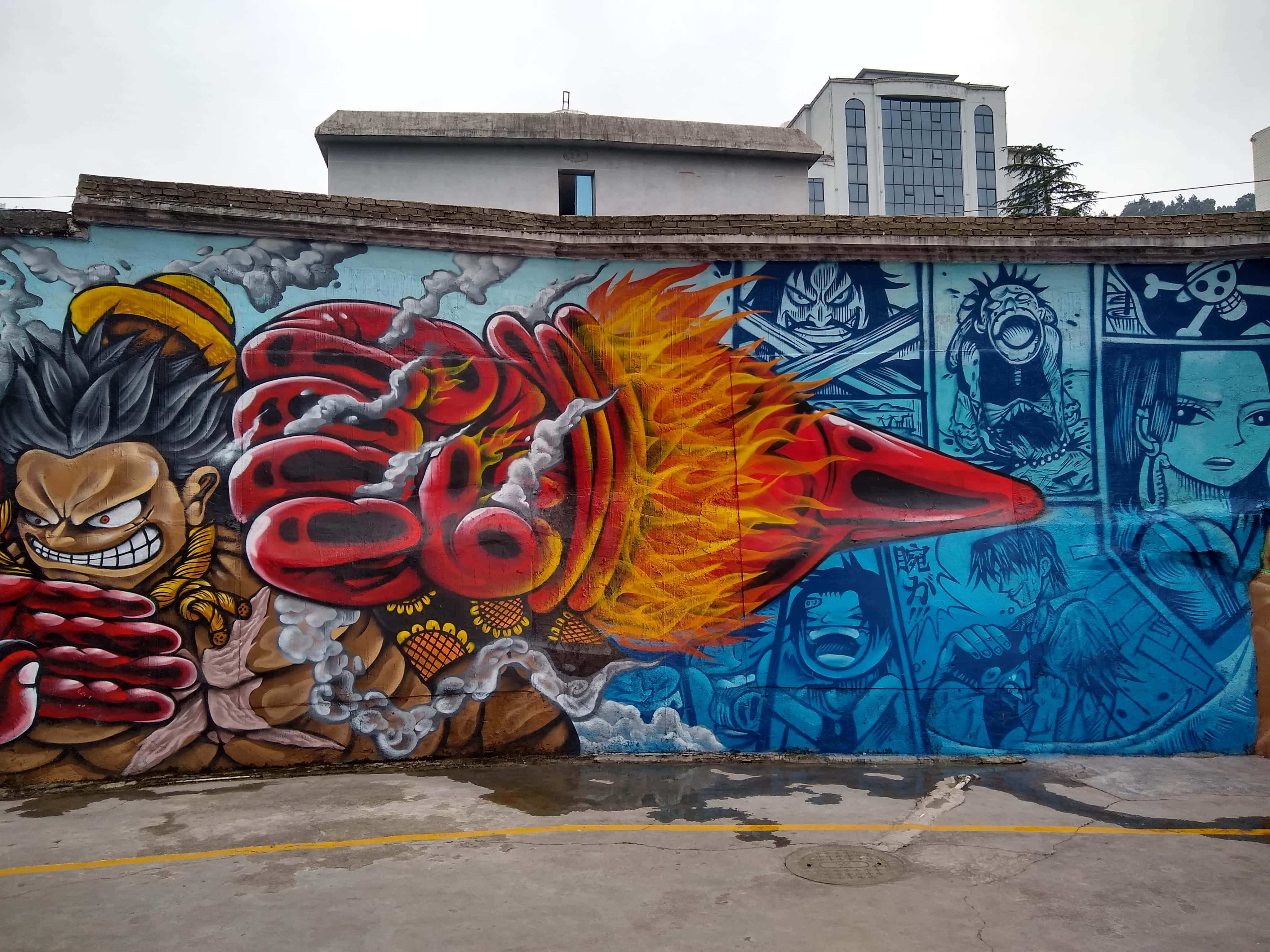 Graffiti Art 桌布 壁紙 — 充滿活力的動漫風格塗鴉壁畫，描繪一個火熱的拳頭擊穿城市小巷中的藍色漫畫面板牆。