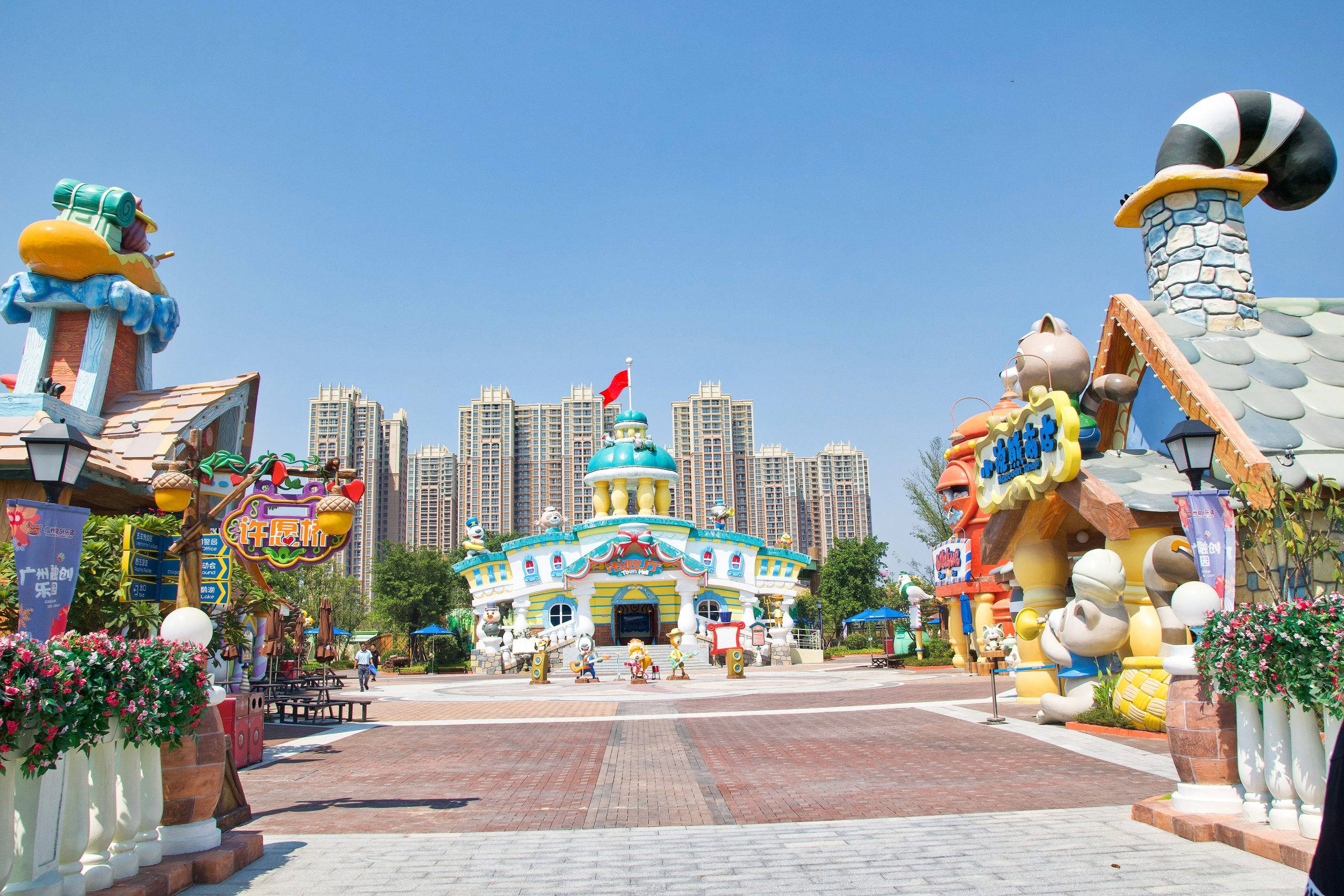 Guangzhou 桌布 壁紙 — 充滿活力的卡通主題遊樂園入口，背景有奇特的建築和現代摩天大樓，在晴朗的藍天下。