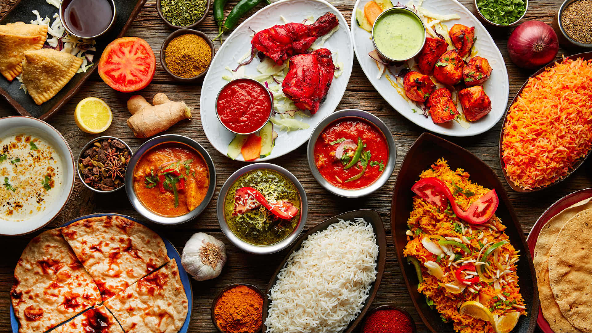 Indian 桌布 壁紙 — 充滿活力的印度菜餚俯視圖，色彩繽紛的咖哩、米飯、印度烤餅和香料擺放在質樸的木桌上。