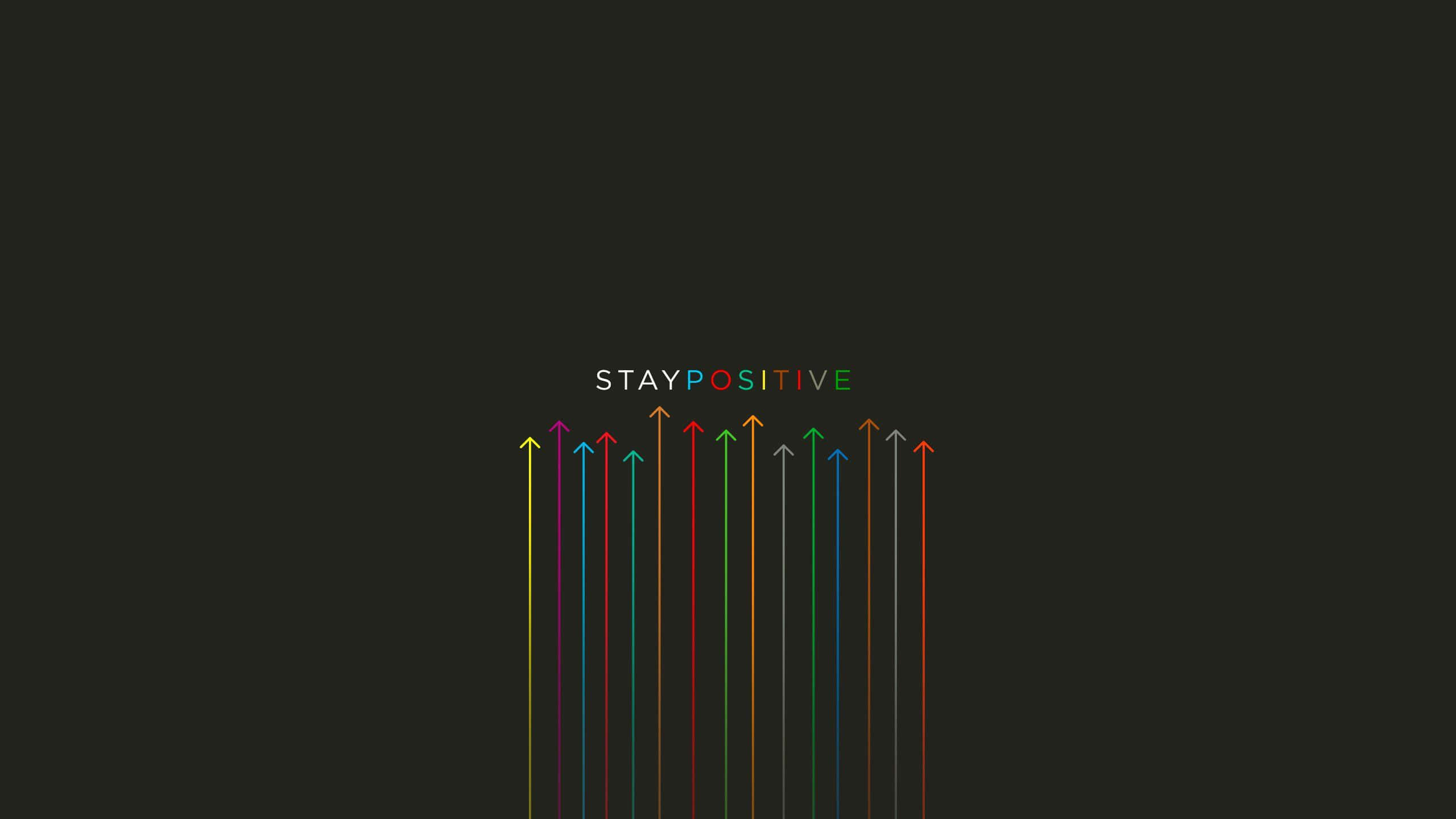 桌布 壁紙 — 充滿活力的向上箭頭以彩虹色調在深色背景上的「STAY POSITIVE」文字下方升起。