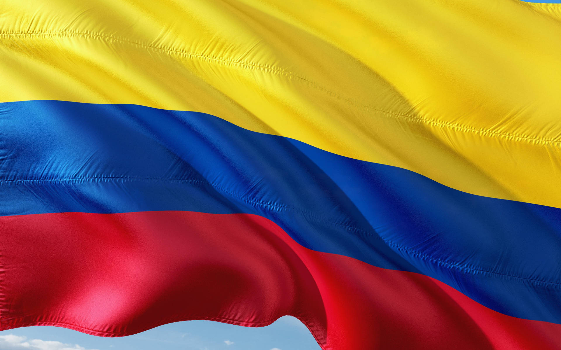 Colombia Flag 桌布 壁紙 — 充滿活力的哥倫比亞國旗，帶有醒目的黃、藍、紅條紋，在清澈的藍天下動態飄揚。