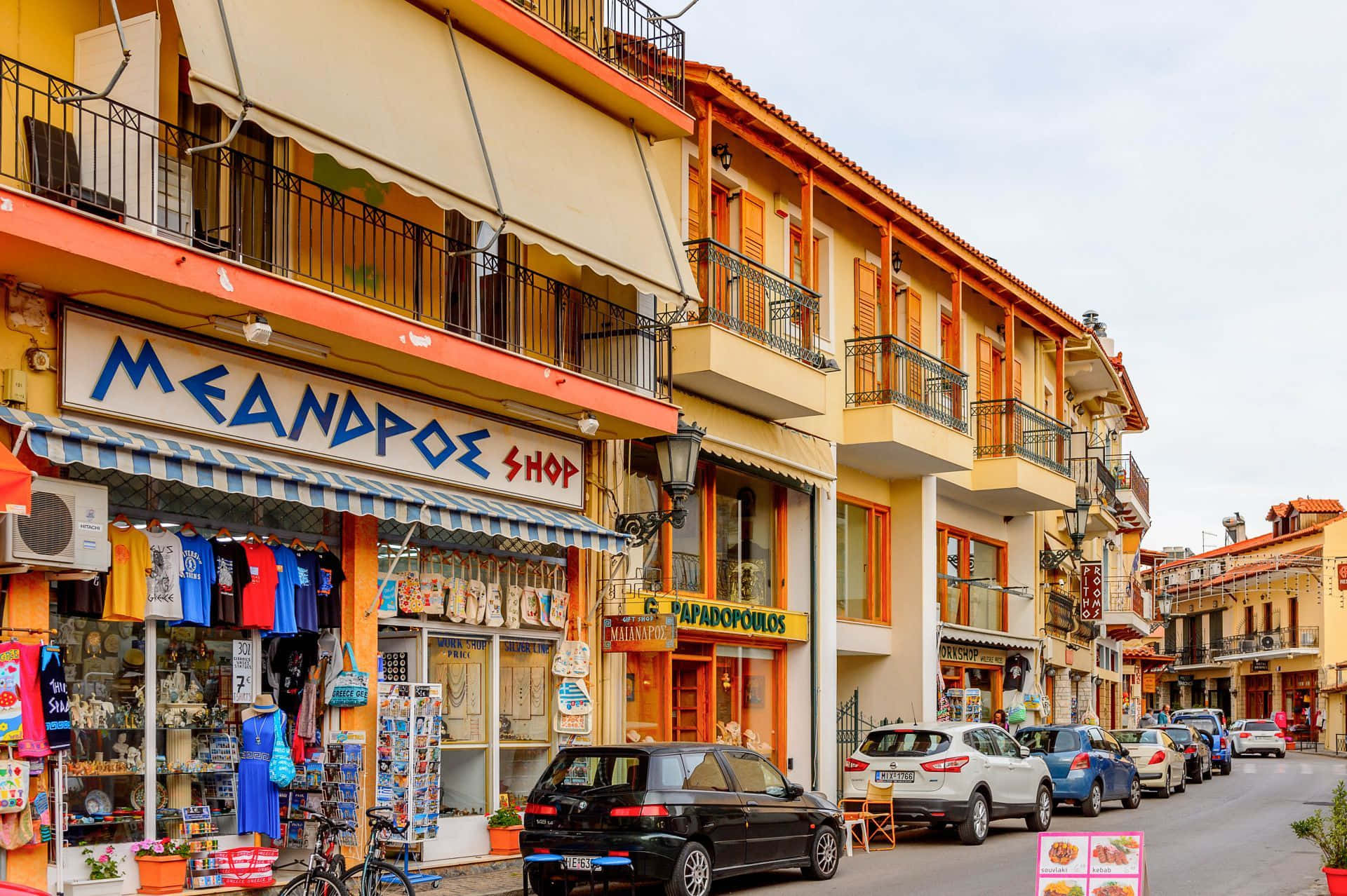 Shopping 桌布 壁紙 — 充滿活力的地中海街道，兩旁是色彩繽紛的商店、陽台和停放的汽車，在柔和日光下。