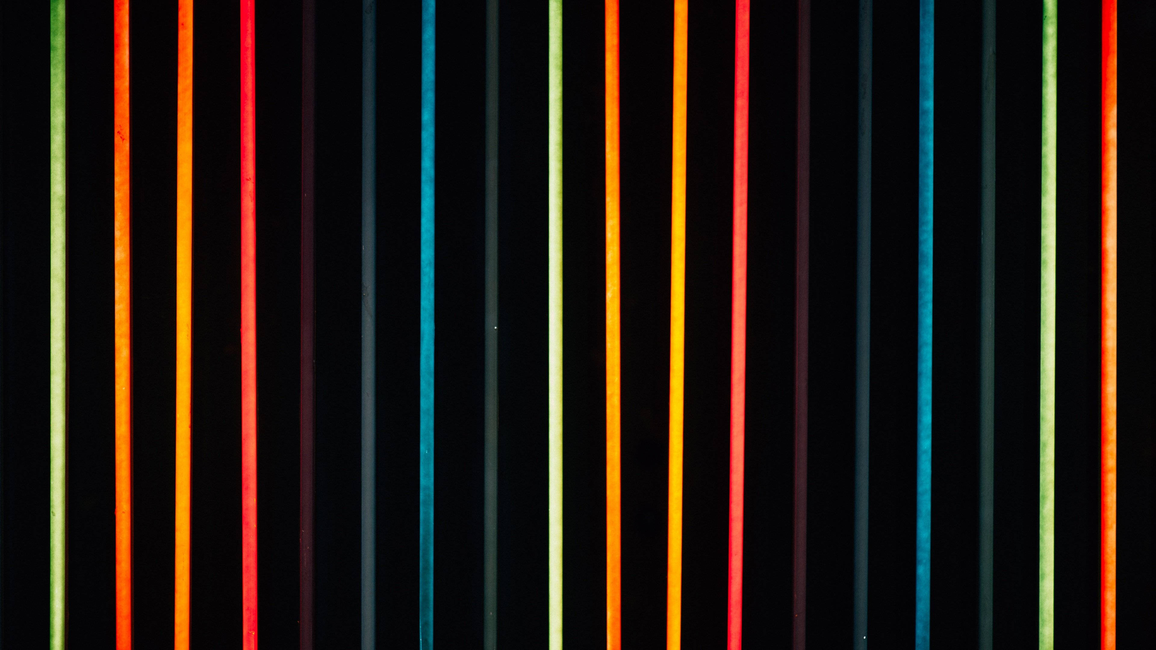 Neon Light 桌布 壁紙 — 充滿活力的垂直霓虹條紋，以紅色、橙色、藍色和綠色在深黑色背景上發光。
