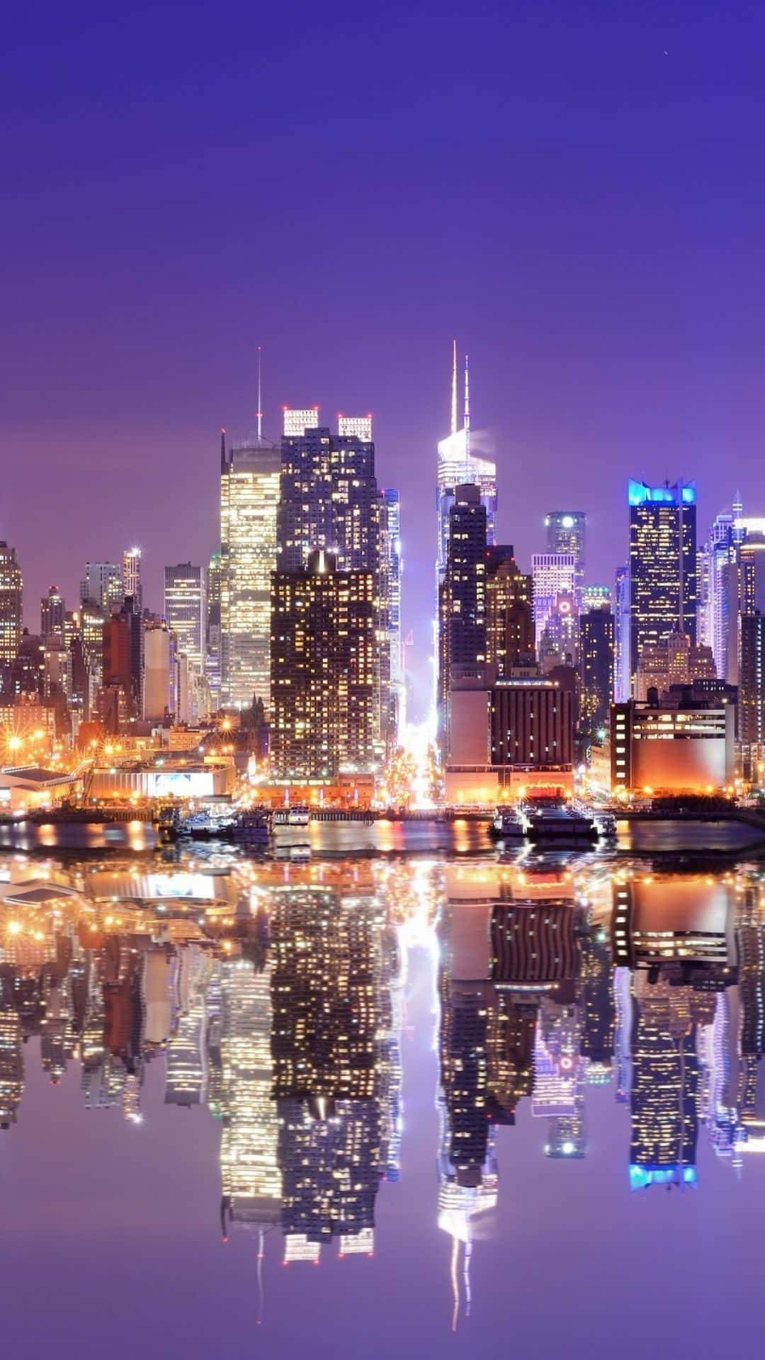 Android Ny City 桌布 壁紙 — 充滿活力的城市夜景，摩天大樓在紫色天空下閃耀，完美倒映在下方平靜的水面上。