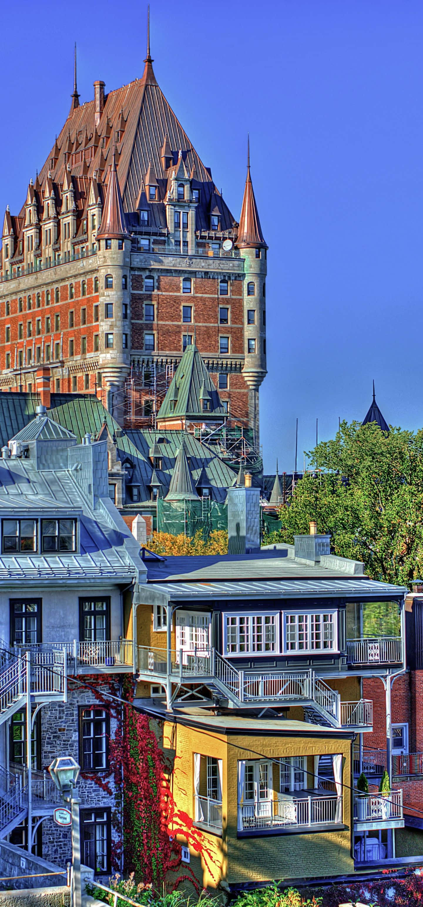 1440x3088 桌布 壁紙 — 充滿活力的城市天際線，以歷史悠久的Château Frontenac為主導，紅磚塔樓和尖頂在清澈的藍天下顯得格外突出。