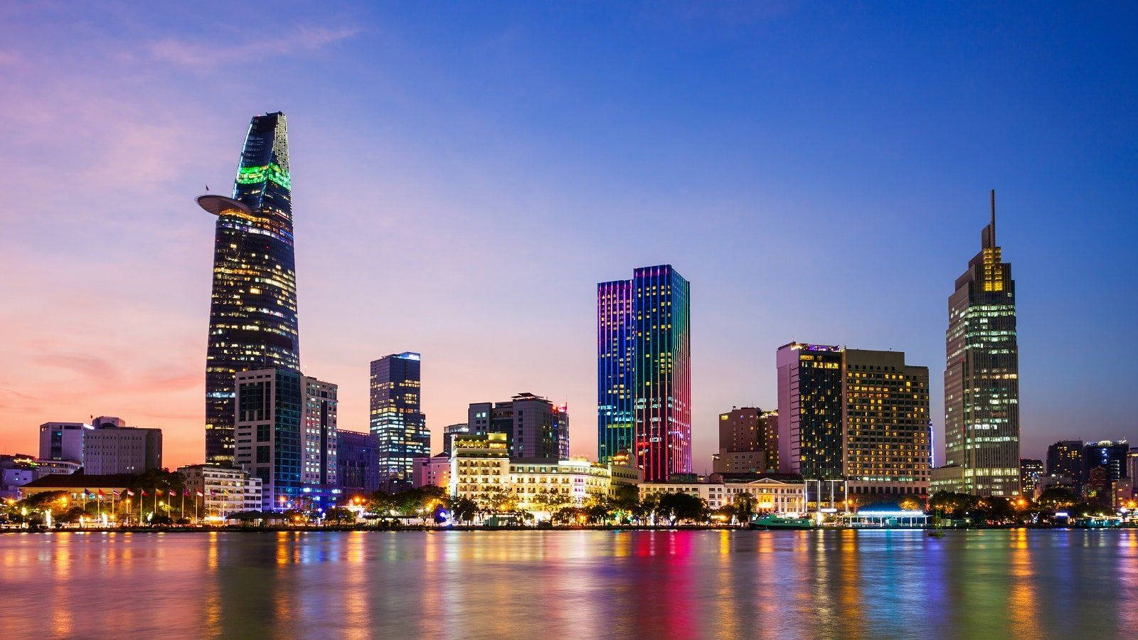 Ho Chi Minh City 桌布 壁紙 — 充滿活力的城市天際線，在黃昏時分，燈火通明的摩天大樓在平靜的水面上倒映，天空呈現漸變色。