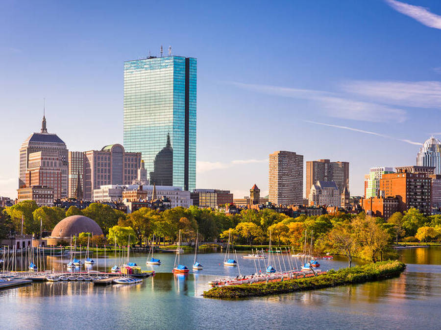 Massachusetts 桌布 壁紙 — 充滿活力的城市天際線，玻璃摩天大樓和帆船停泊在平靜的河流中，周圍是秋天的樹木，在清澈的藍天下。