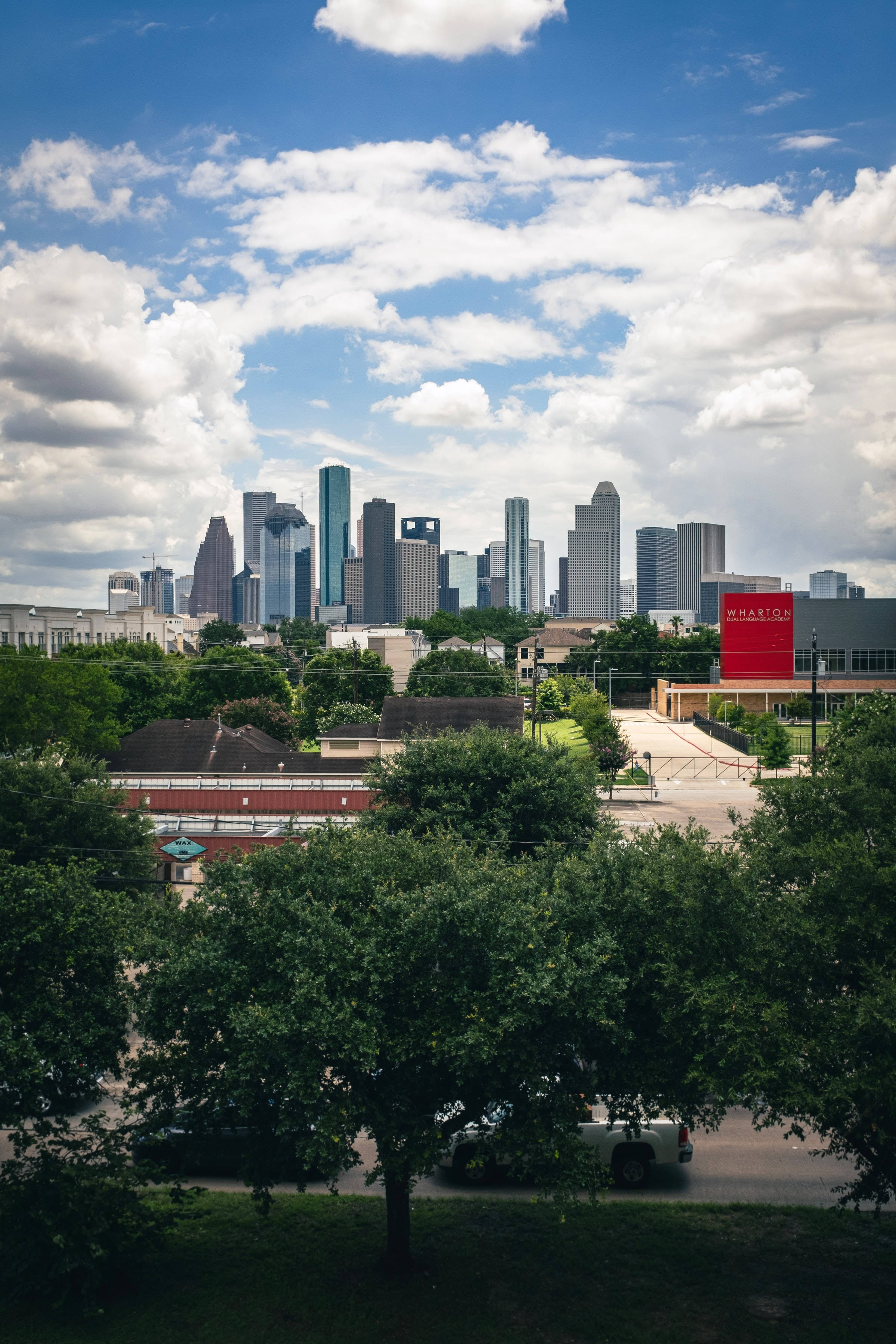 Houston 桌布 壁紙 — 充滿活力的城市天際線，現代摩天大樓在茂密的綠樹上方升起，藍天白雲點綴其間。