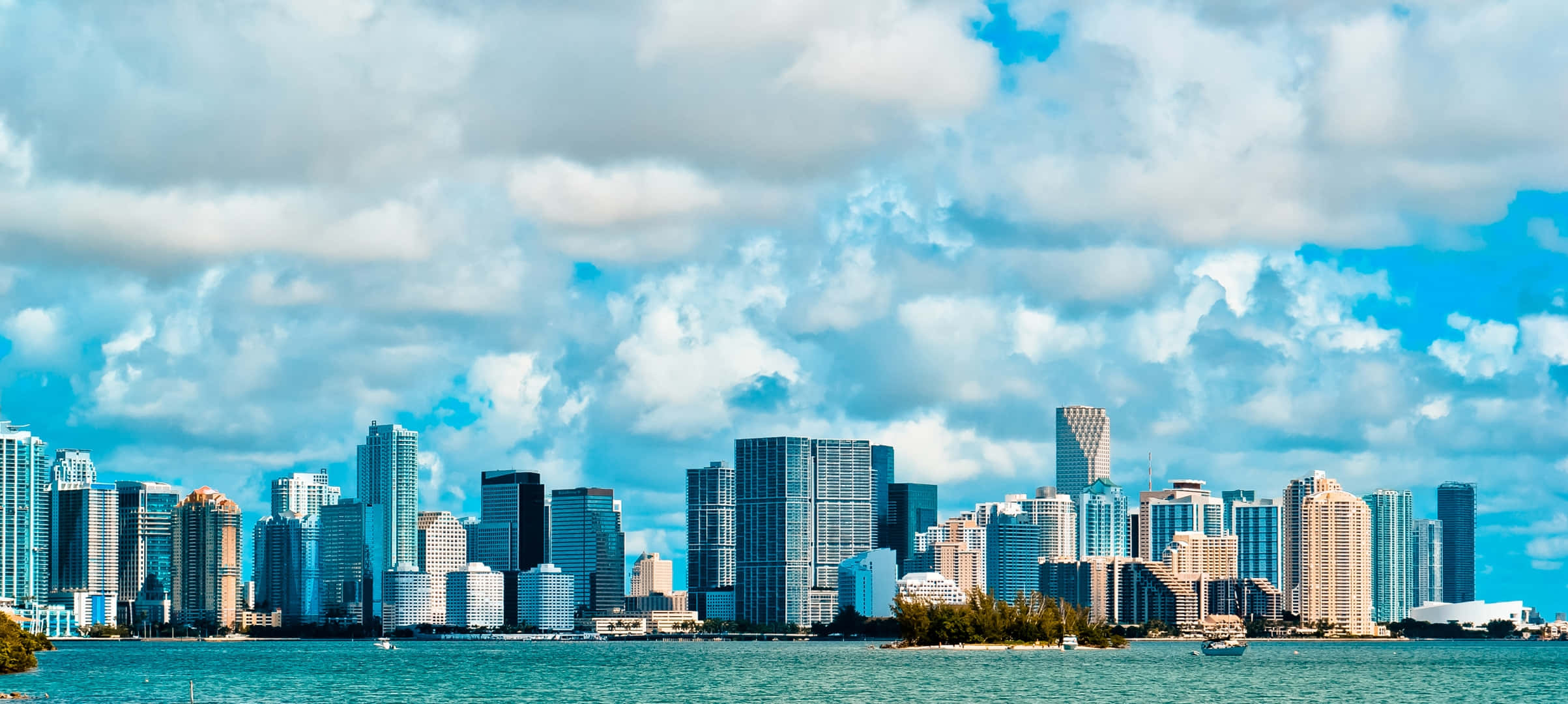florida 桌布 壁紙 — 充滿活力的城市天際線，現代摩天大樓從碧綠色的海水中升起，在佈滿蓬鬆白雲的明亮藍天下。