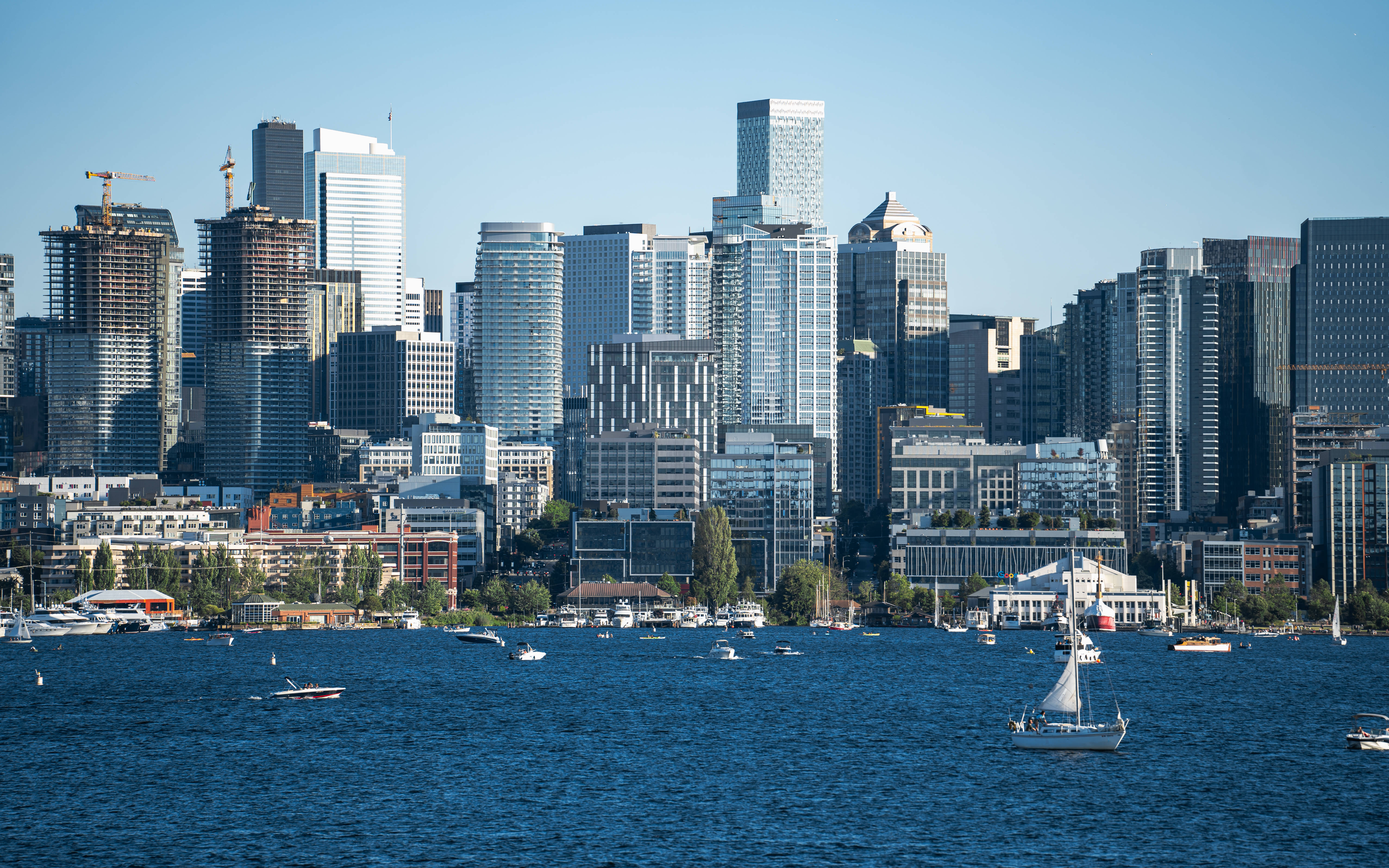 seattle 4K 桌布 壁紙 — 充滿活力的城市天際線，現代摩天大樓和建築起重機聳立在繁忙的港口之上，港口中滿是帆船和機動船，天空清澈湛藍。