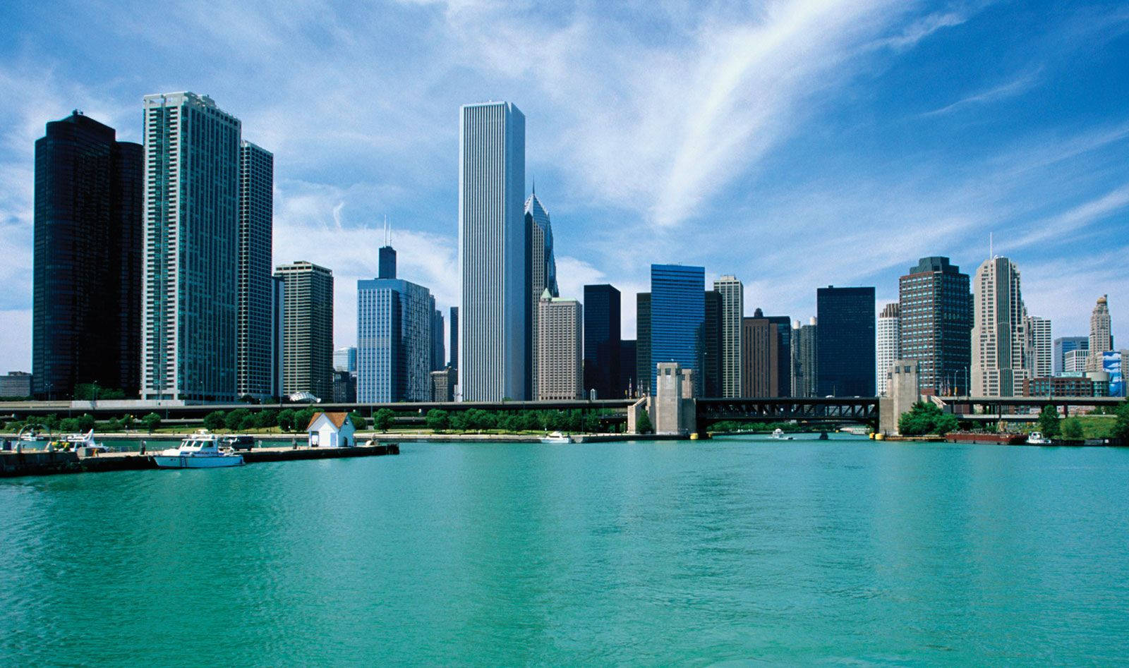 Illinois 桌布 壁紙 — 充滿活力的城市天際線，高聳的摩天大樓倒映在碧綠的水面上，明亮的藍天中飄著縷縷白雲。