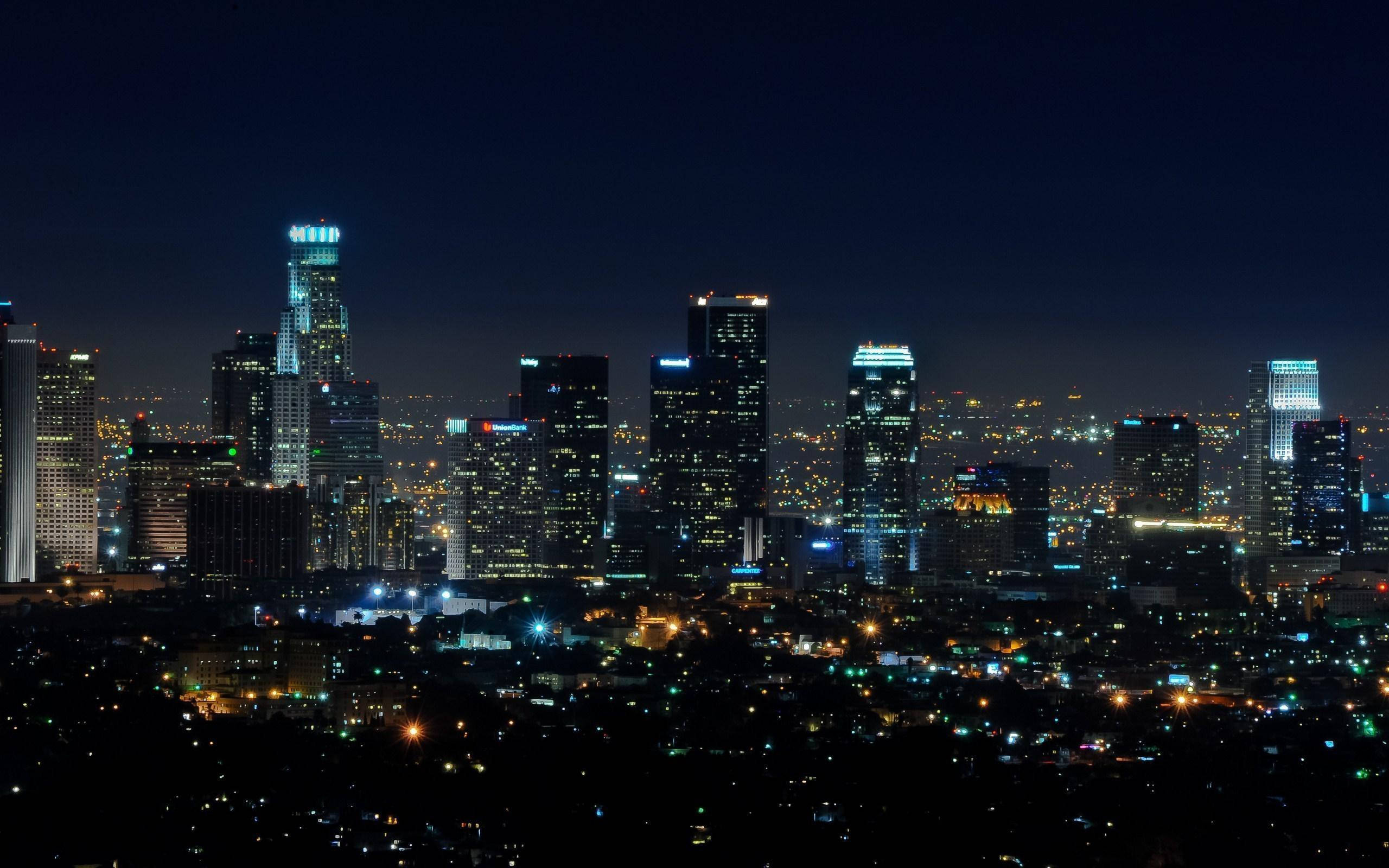 城市 桌布 壁紙 — 充滿活力的城市天際線全景夜景，高聳的摩天大樓在深藍色天空的映襯下閃耀。