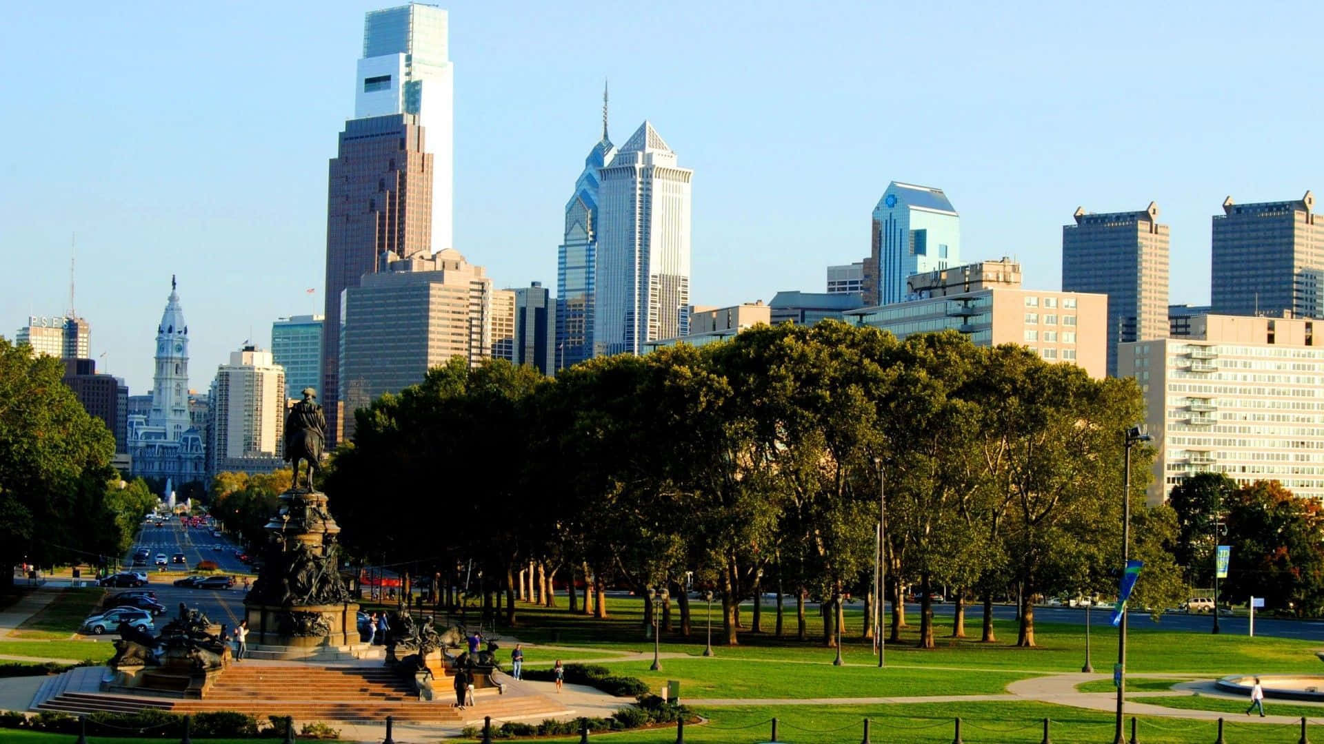Philly 桌布 壁紙 — 充滿活力的城市天際線在一個綠意盎然的公園後面升起，公園中央有一座騎馬雕像和蜿蜒的小徑。