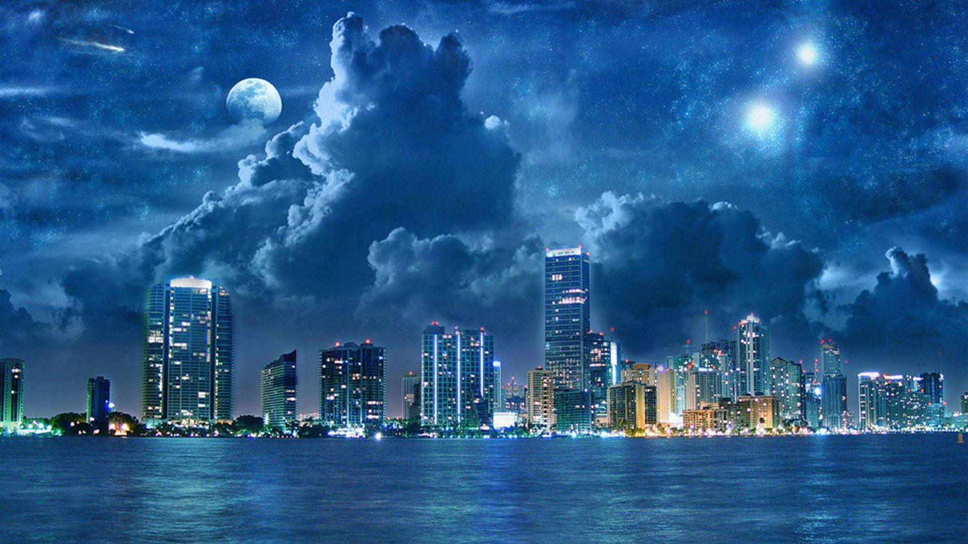 桌布 壁紙 — 充滿活力的城市天際線在夜晚倒映在水中，天空佈滿星星和戲劇性的雲彩，月光照耀。