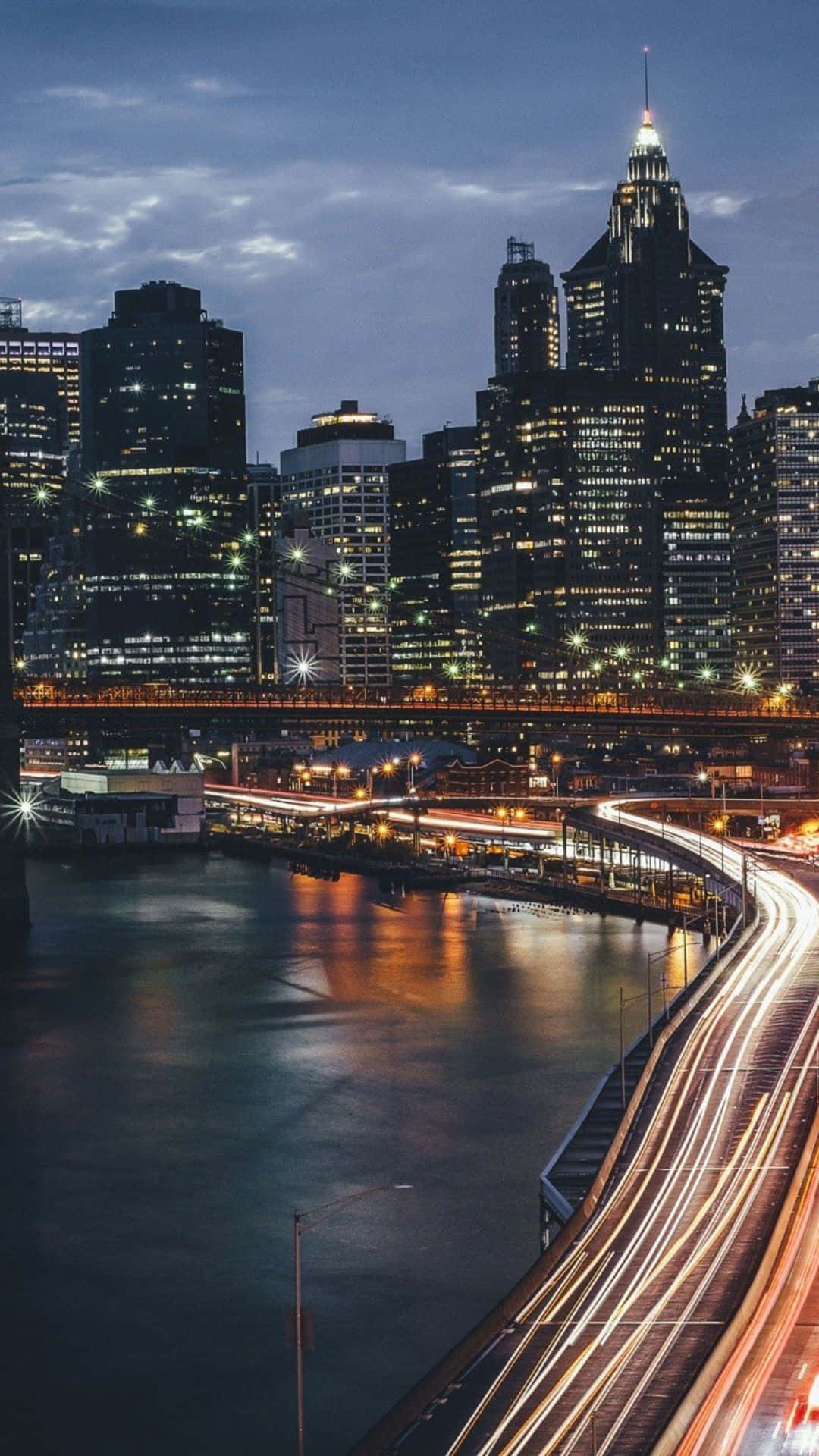 Android Ny City 桌布 壁紙 — 充滿活力的城市天際線在黃昏時分，閃爍的摩天大樓和河岸高速公路上的車流光跡。
