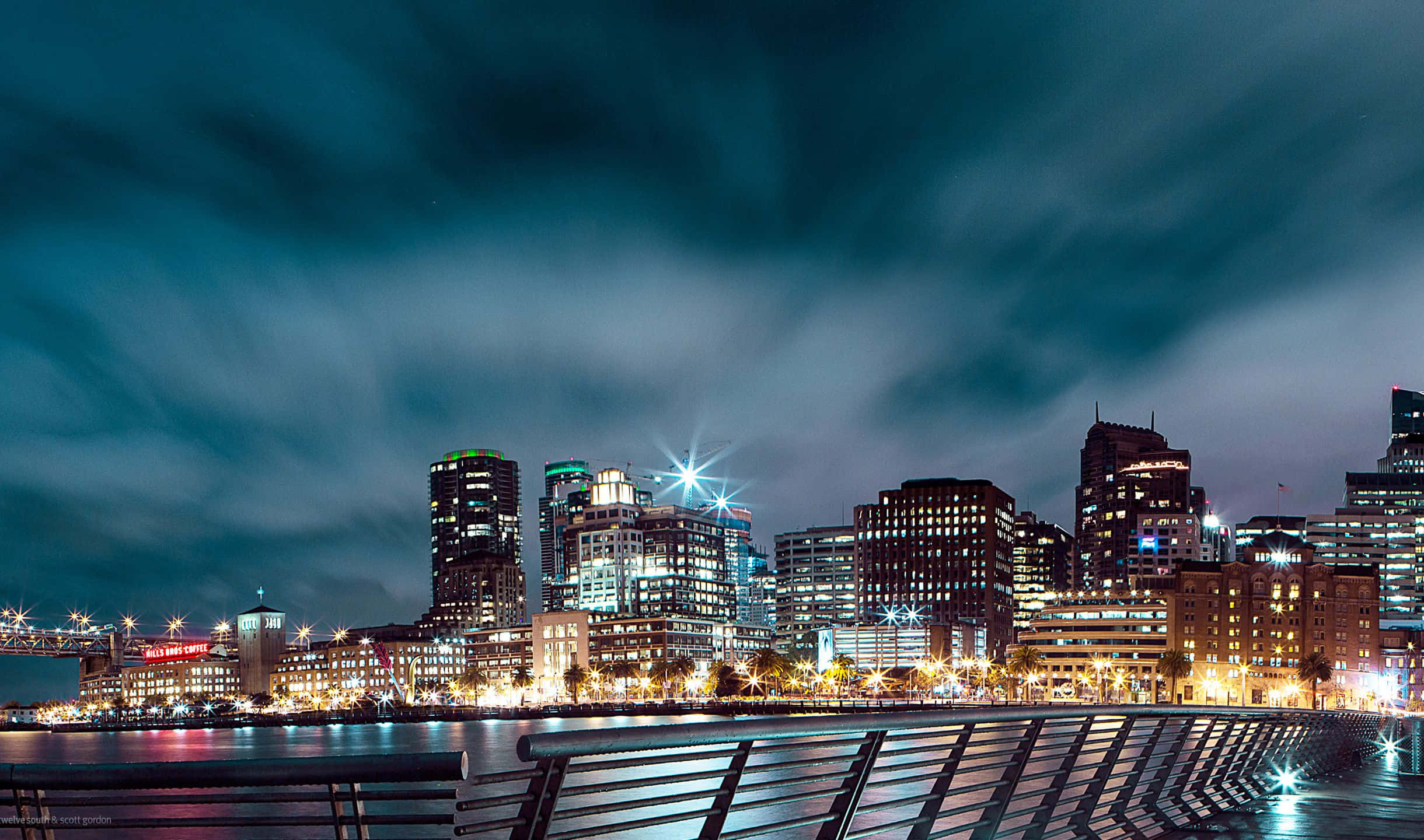 2440x1440 San Francisco 桌布 壁紙 — 充滿活力的城市天際線夜景，發光的摩天大樓倒映在平靜的水面上，天空多雲而戲劇化。