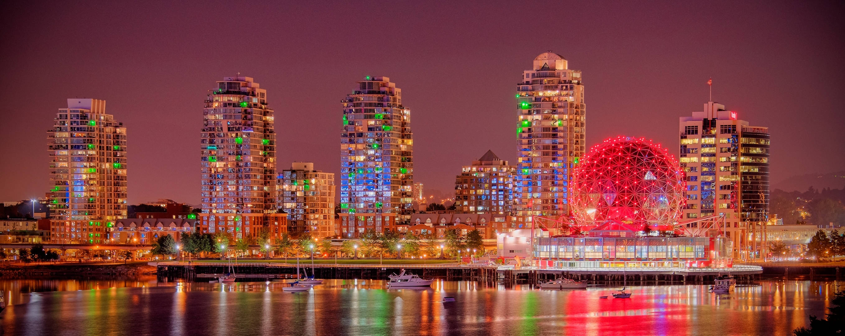 lights 桌布 壁紙 — 充滿活力的城市天際線夜景，色彩繽紛的摩天大樓和發光的紅色球形結構倒映在平靜的水面上。