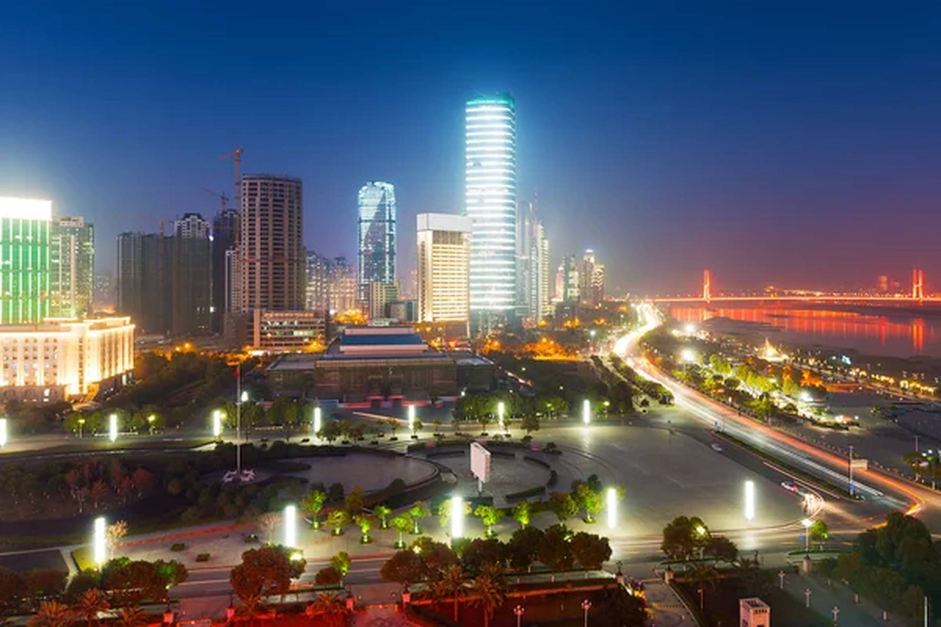Wuhan 桌布 壁紙 — 充滿活力的城市天際線夜景，閃爍的摩天大樓和一座點亮的橋樑橫跨河流，反射出溫暖的燈光。