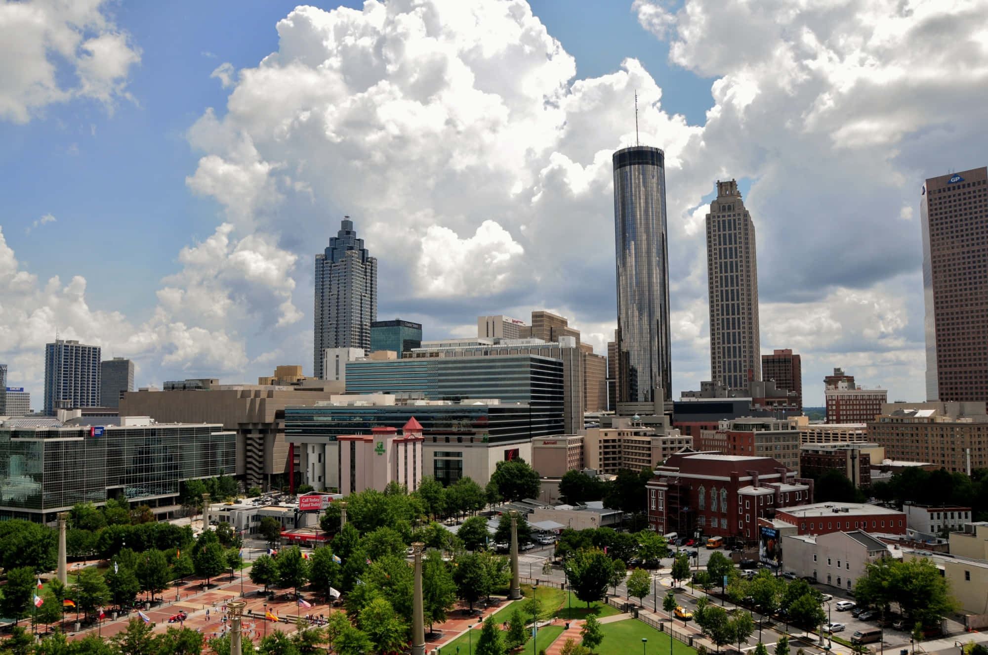 Atlanta Georgia 桌布 壁紙 — 充滿活力的城市景觀，擁有現代摩天大樓和茂密的綠色公園，在明亮的藍天和蓬鬆的白雲下。