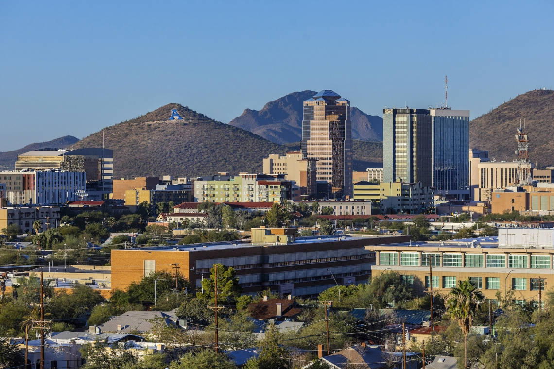 Arizona 桌布 壁紙 — 充滿活力的城市景觀，現代摩天大樓和低層建築坐落在乾燥的山脈之間，天空清澈湛藍。
