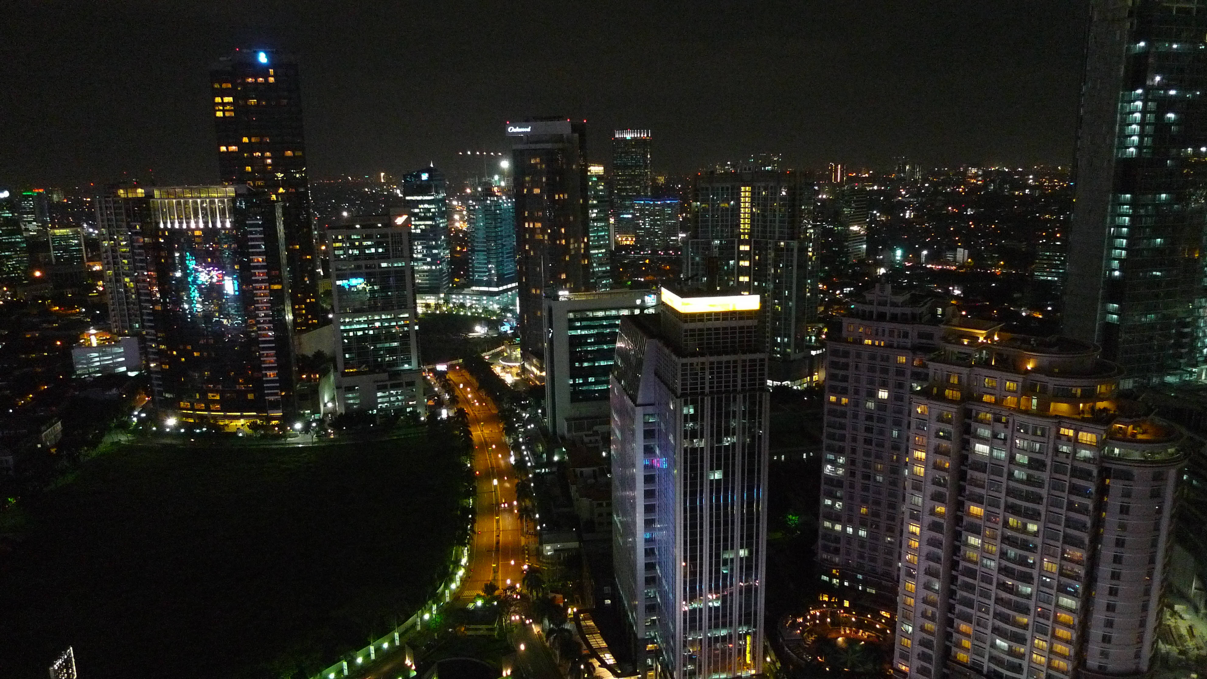 Jakarta 桌布 壁紙 — 充滿活力的城市景觀的夜間鳥瞰圖，閃爍的摩天大樓和燈火通明的街道蜿蜒穿過密集的城市建築。