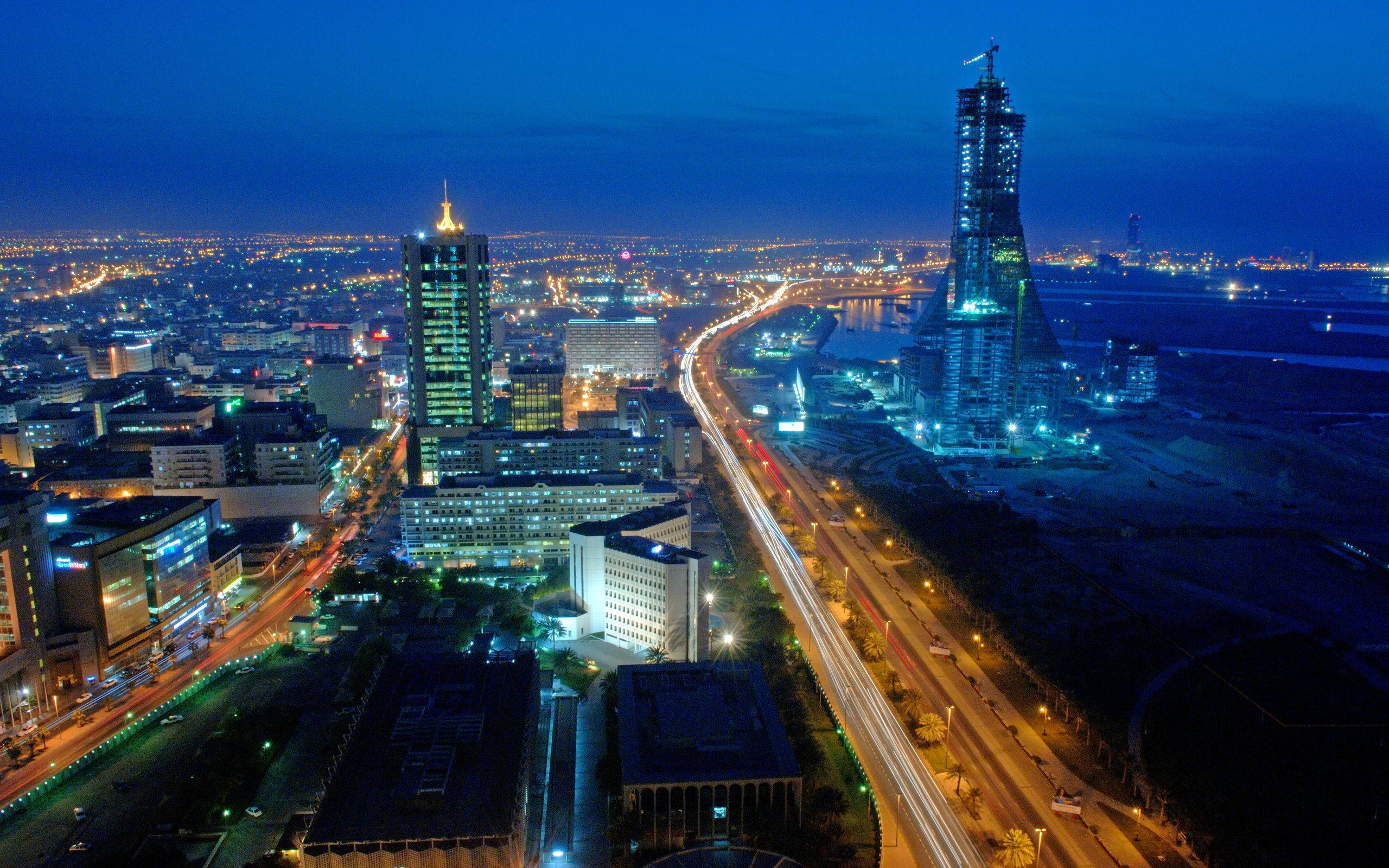 Bahrain 桌布 壁紙 — 充滿活力的城市景觀的空中夜景，閃爍的摩天大樓和蜿蜒道路上交通留下的光跡。